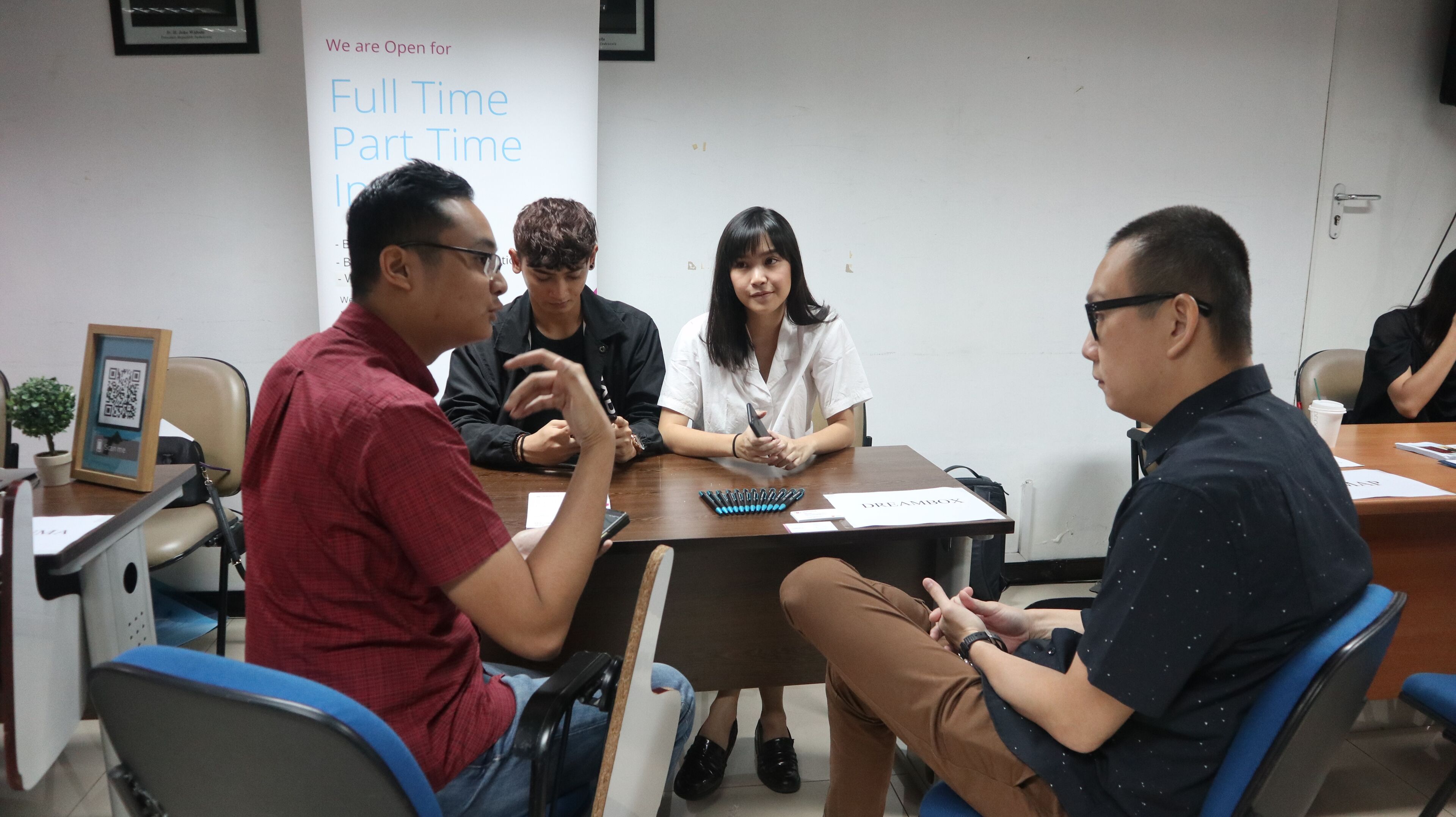 Four professionals engaged in a discussion at a table with pens and documents, under a sign that reads "Full Time Part Time Intern".