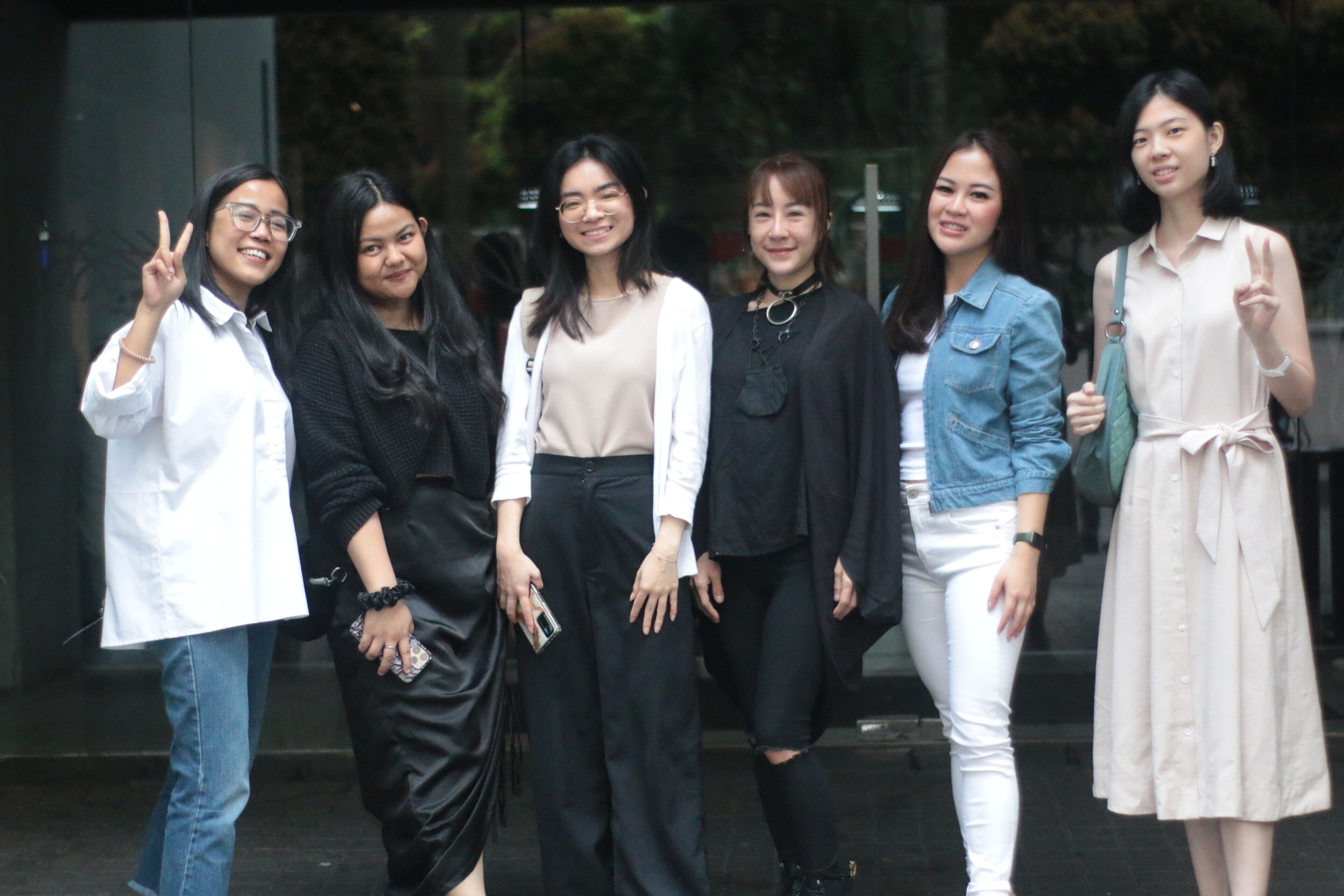 ix smiling women standing together outdoors, displaying peace signs and casual fashion styles.