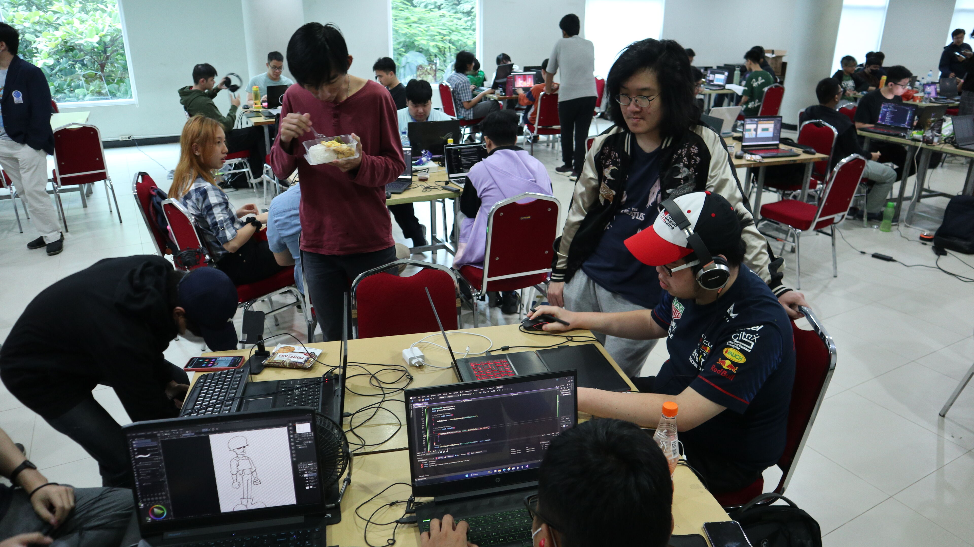 Participants are deeply engaged in programming at a hackathon event, with laptops and screens displaying code in a busy hall.

