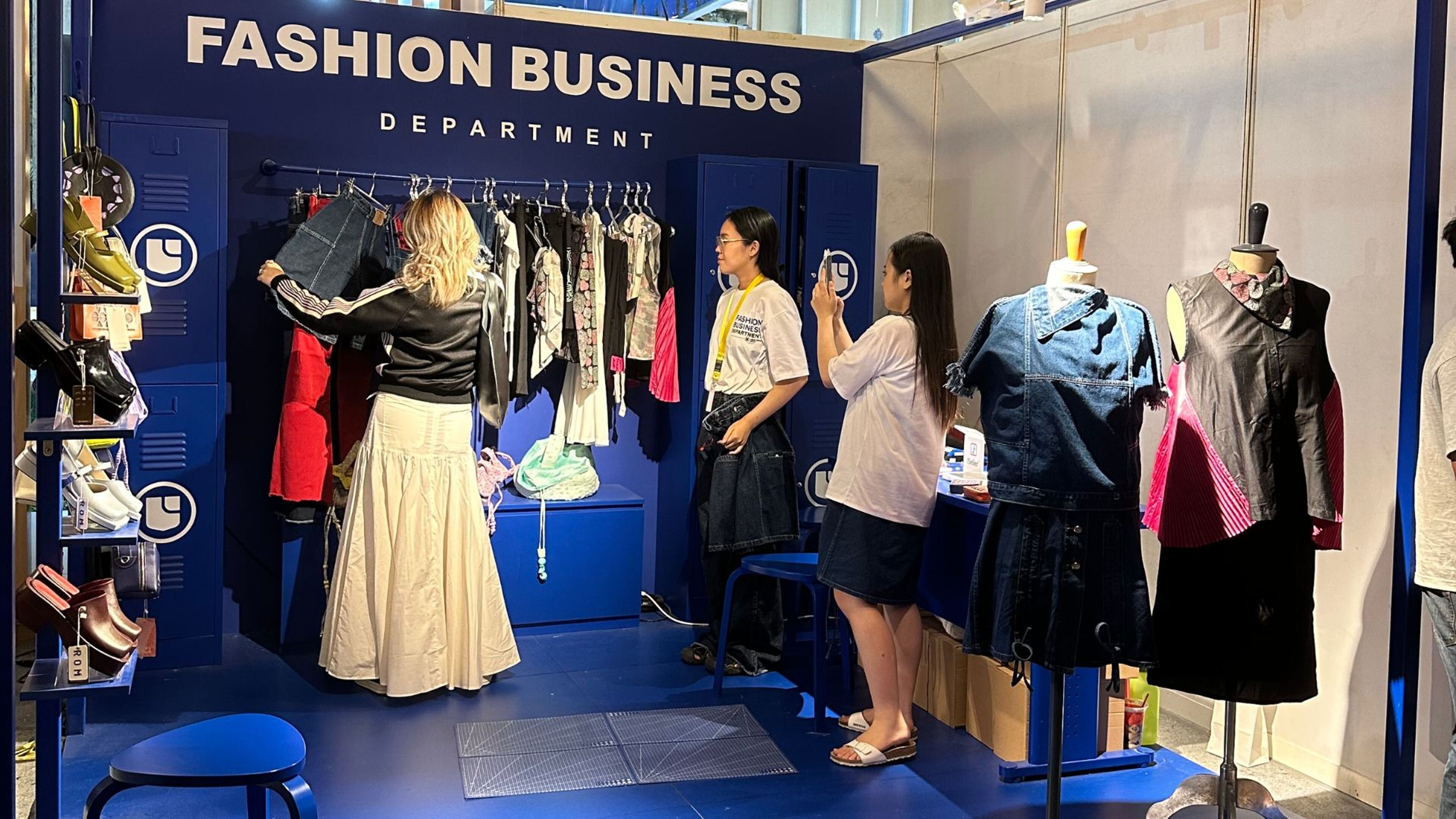 Attendees explore a fashion business department exhibit, examining various garments and accessories on display.