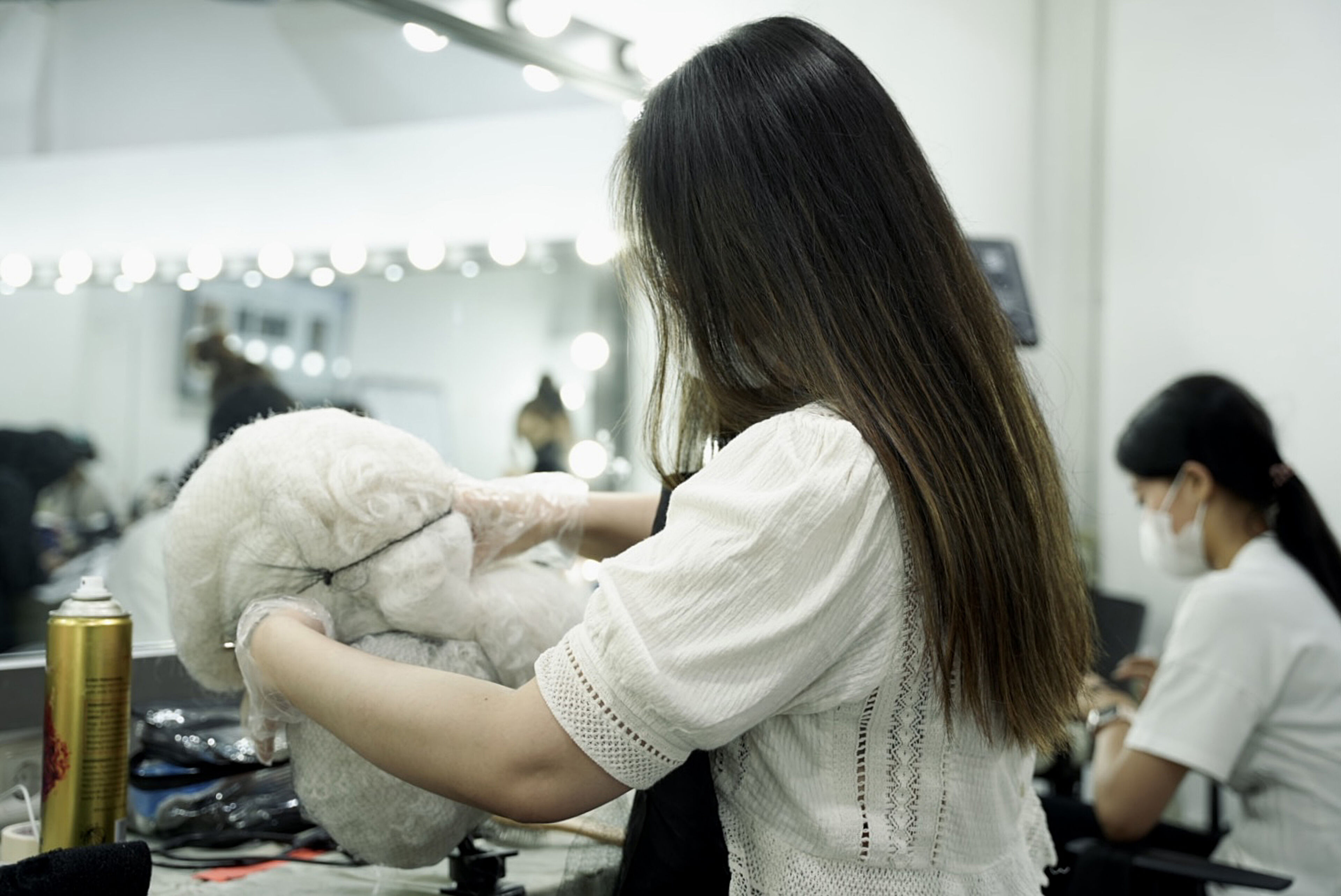A focused hairstylist secures a voluminous wig on a stand, preparing it for styling in a salon setting.