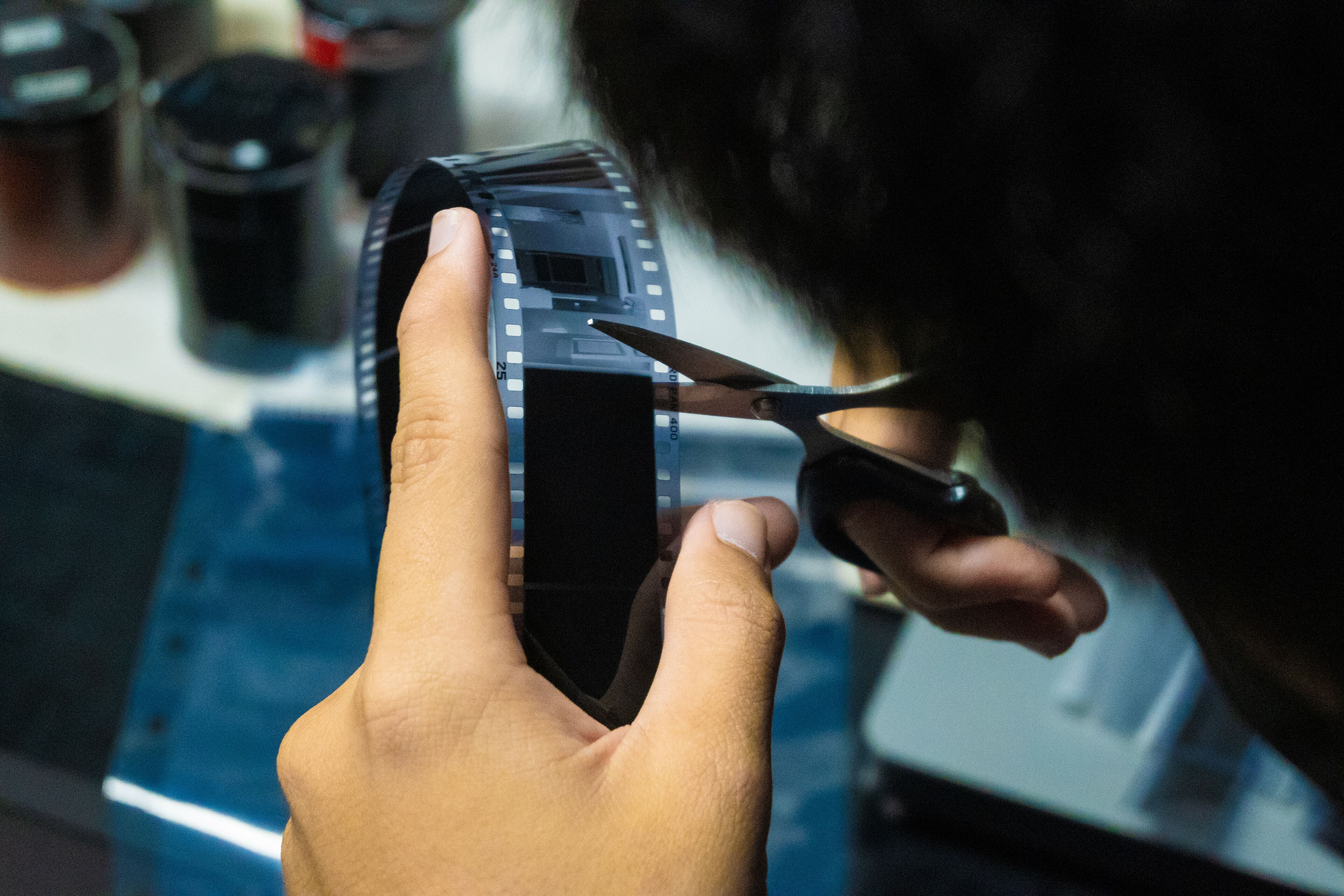 A person closely examines a strip of film negatives with scissors, potentially for editing or archiving.