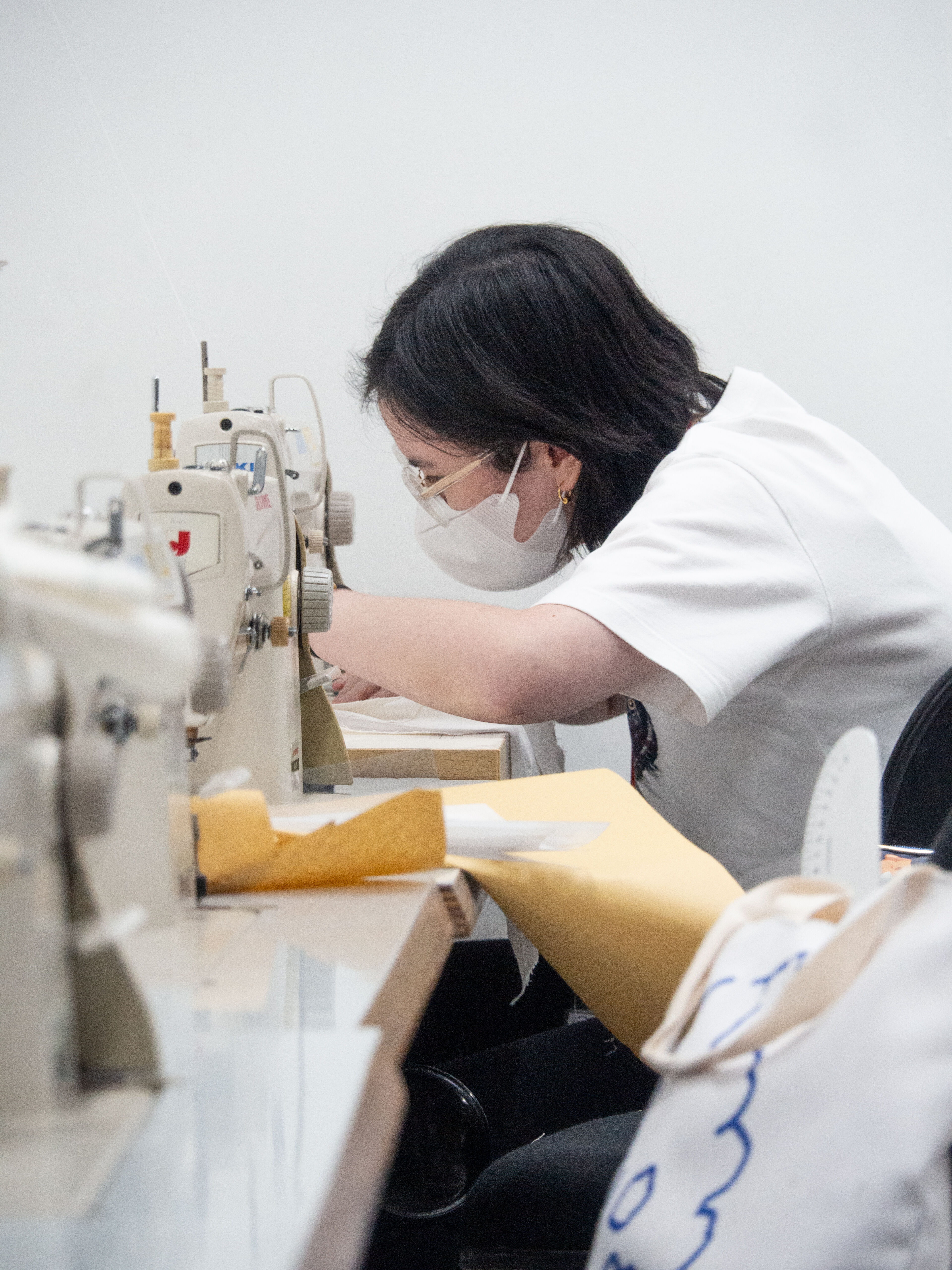 A focused tailor sewing with an industrial machine, fabric pieces on her workstation.