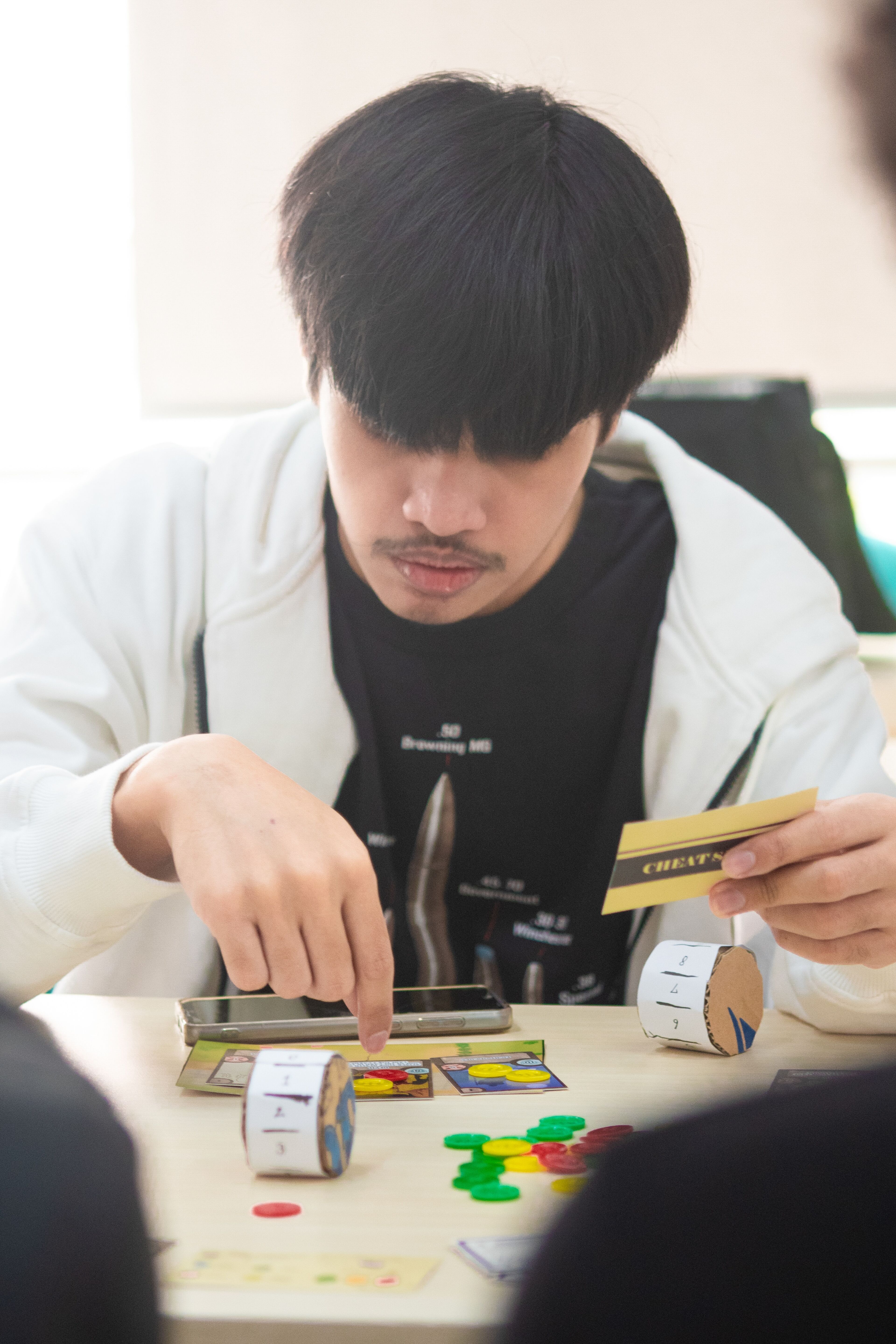 A focused individual engaging in a strategic board game, contemplating his next move with various game pieces and cards on the table.