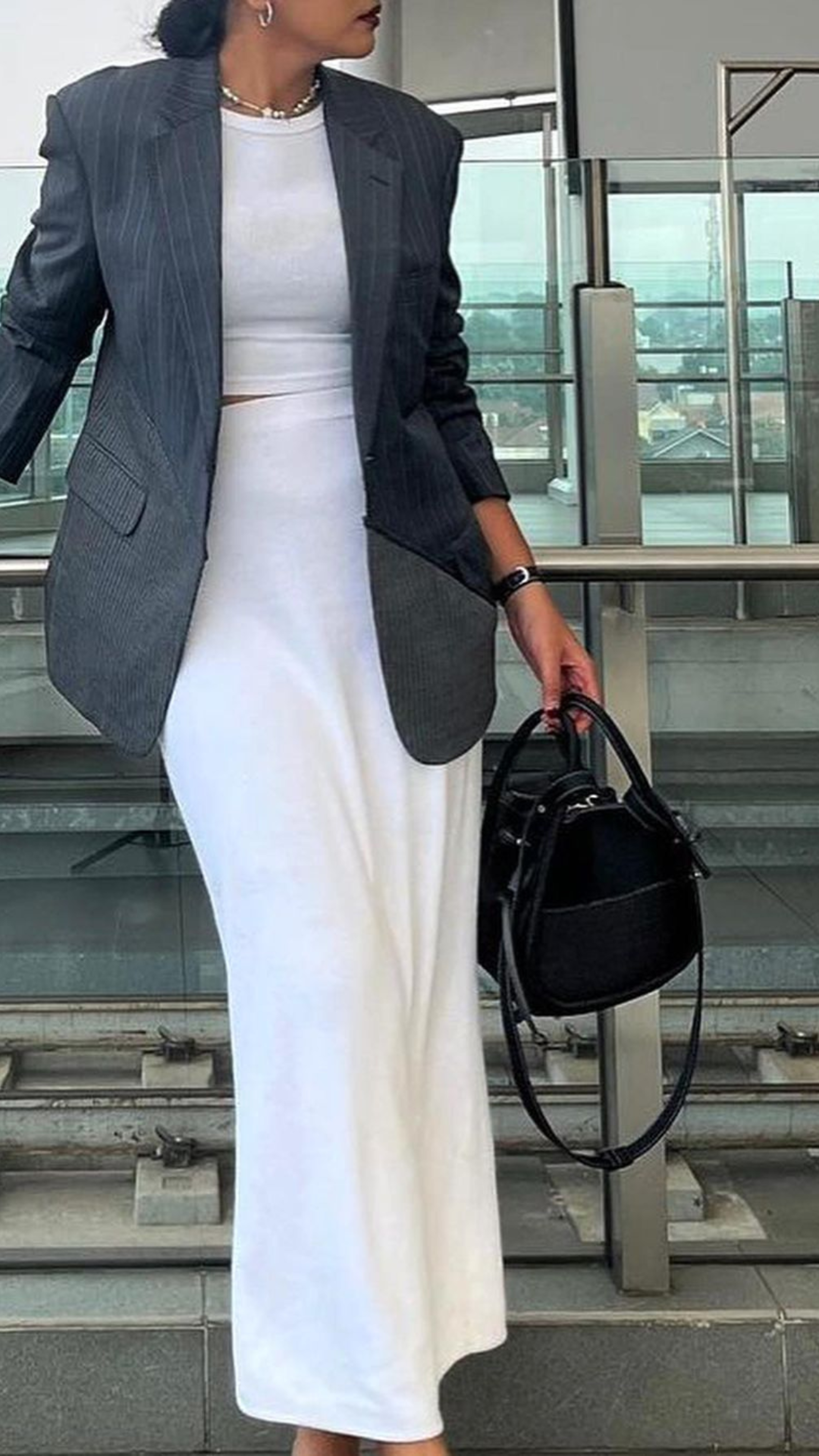 A sophisticated ensemble featuring a pinstripe blazer and sleek white dress paired with a black Josvli handbag, epitomizing contemporary elegance.