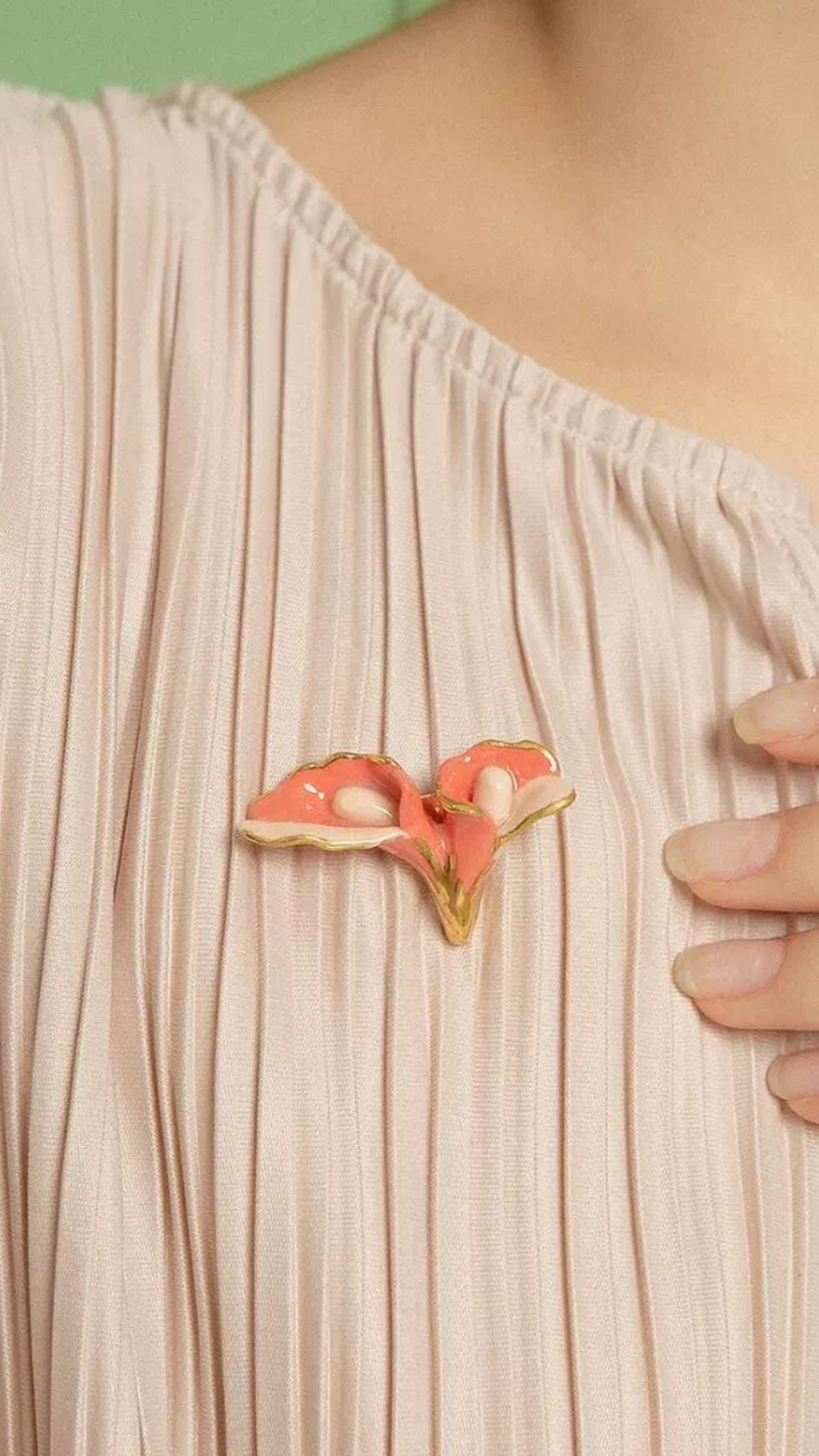 A delicate coral floral brooch with gold trim accents pinned on a pleated blush blouse.