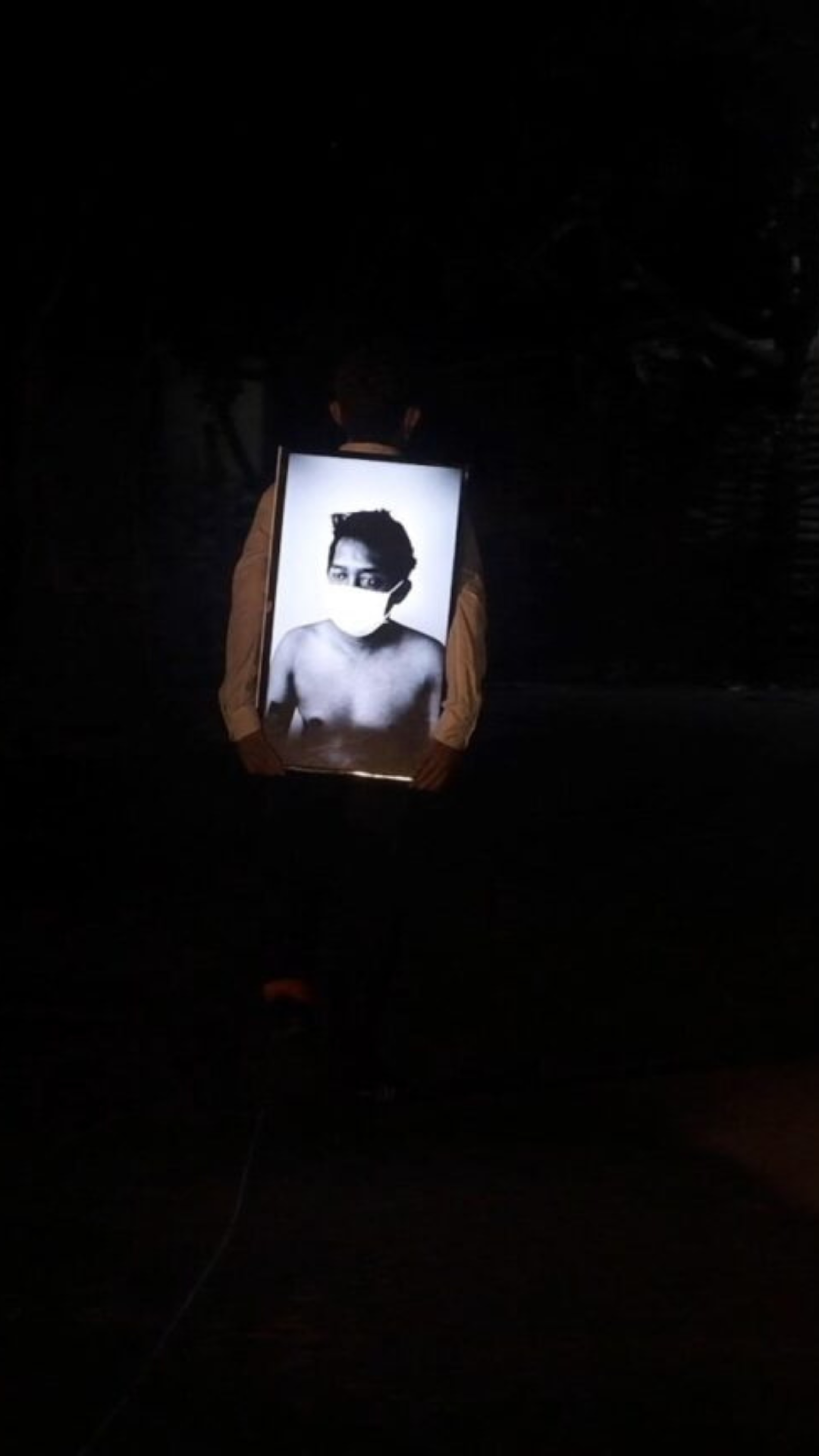 A person holding a backlit framed portrait in the dark.