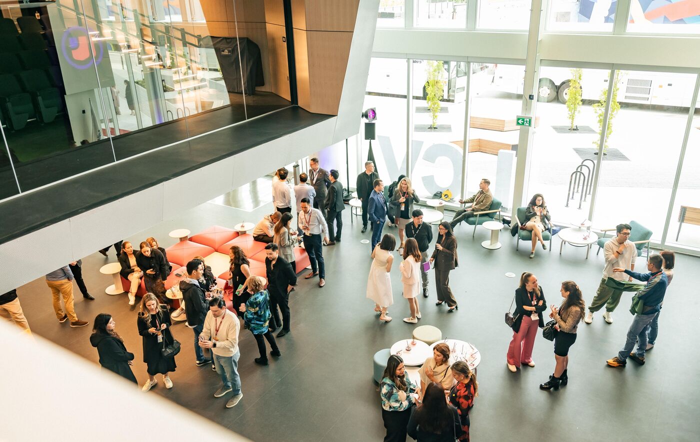 High-angle view of a modern, open-plan office space with numerous people mingling and standing in small groups.