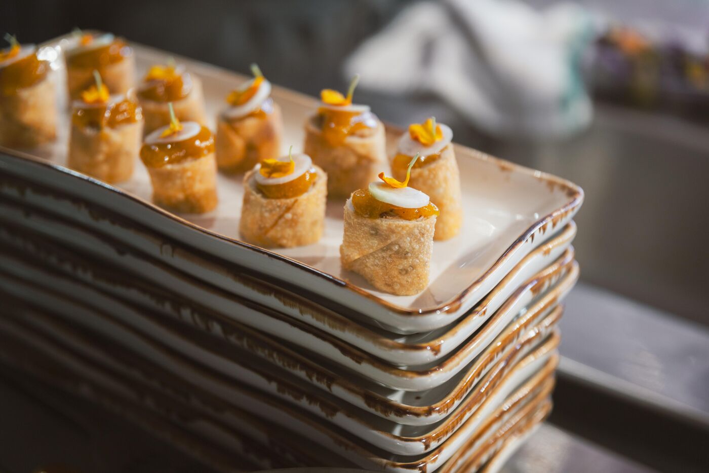 This image displays a rectangular platter filled with puff pastry-wrapped appetizers, topped with a glossy glaze and garnished with a small flower and a dollop of cheese or cream.