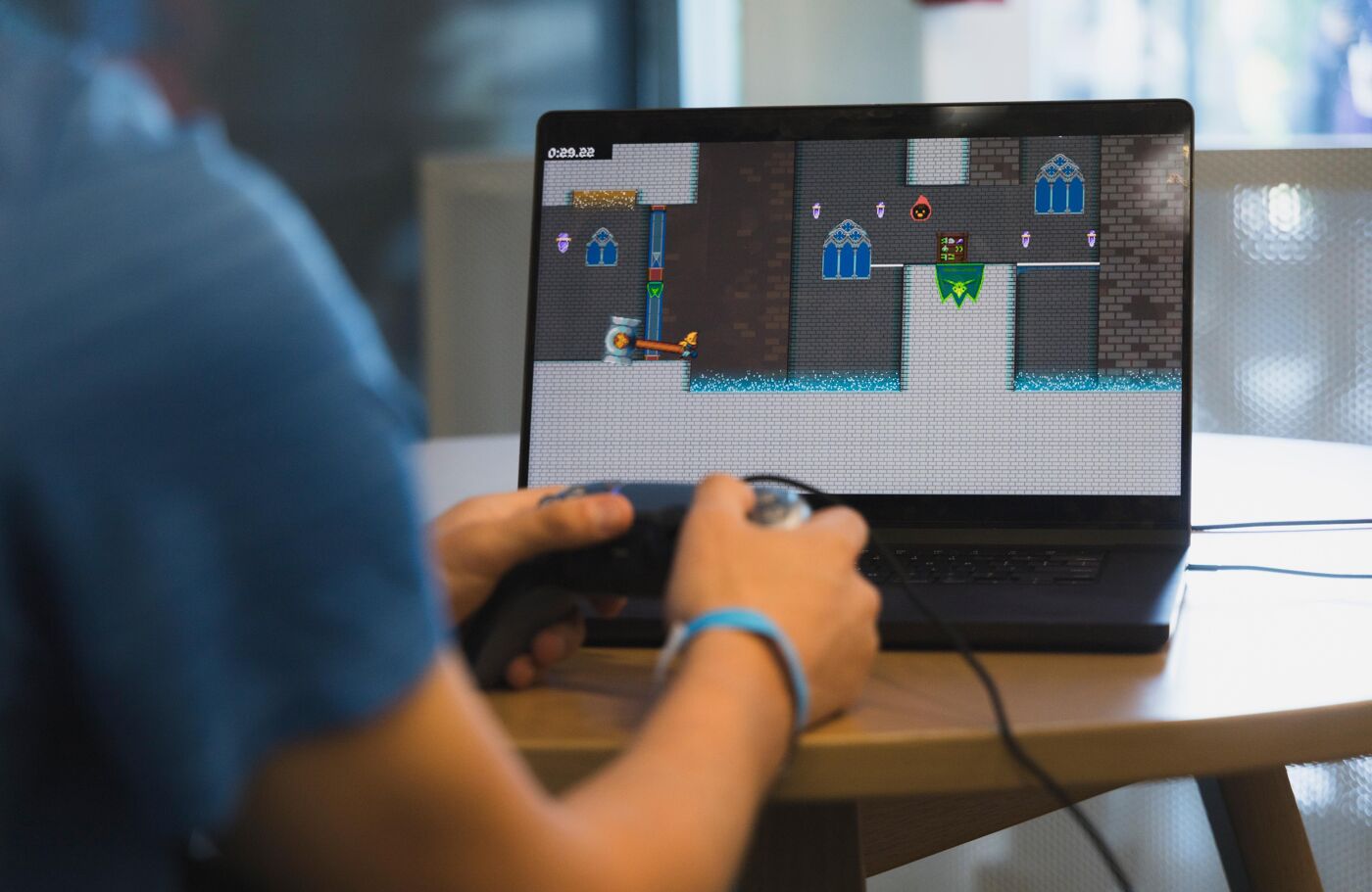 A person is playing a computer game with a controller. The game features retro graphics and appears to be a platformer with puzzle elements.