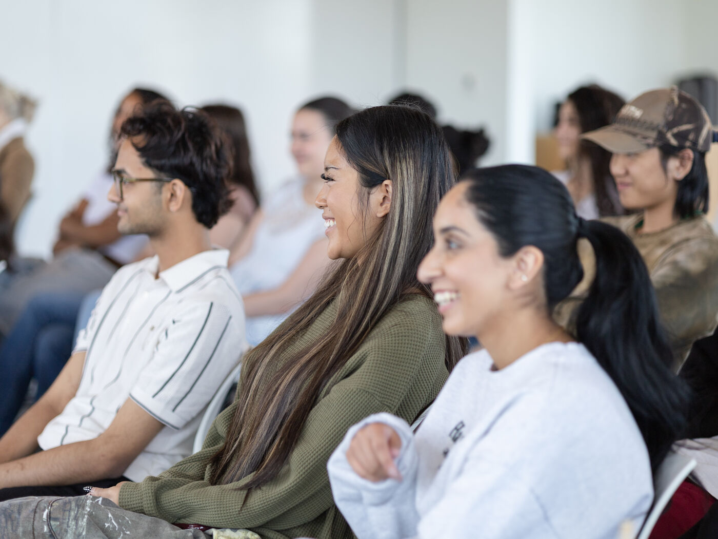 A group of smiling students attend a lecture or presentation, seated together in a common area.