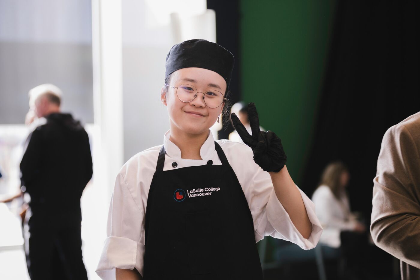 A person wearing a chef's hat and apron is making a peace sign with their hand.