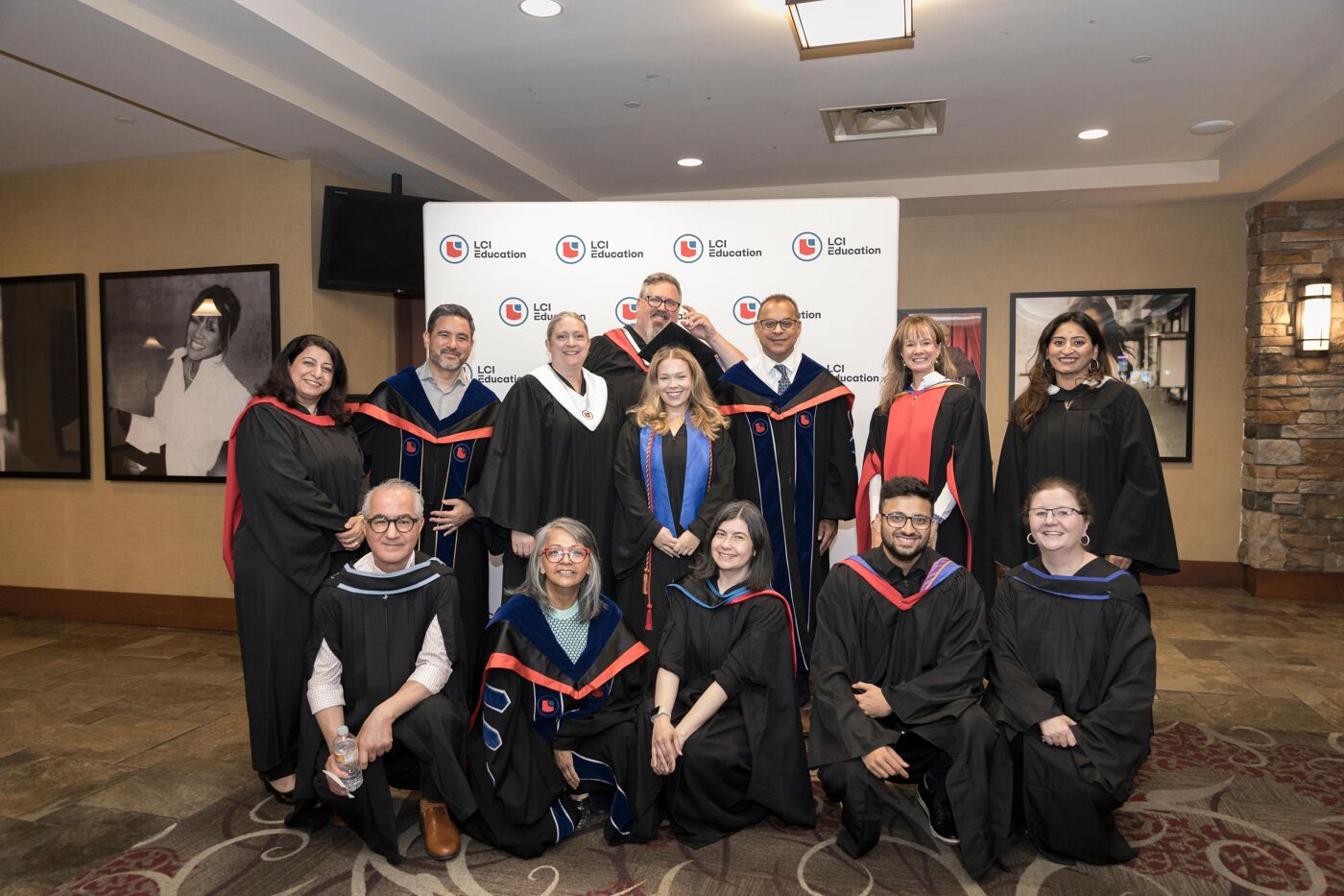 A group of graduates and faculty pose for a group photo, all dressed in academic regalia and caps.
