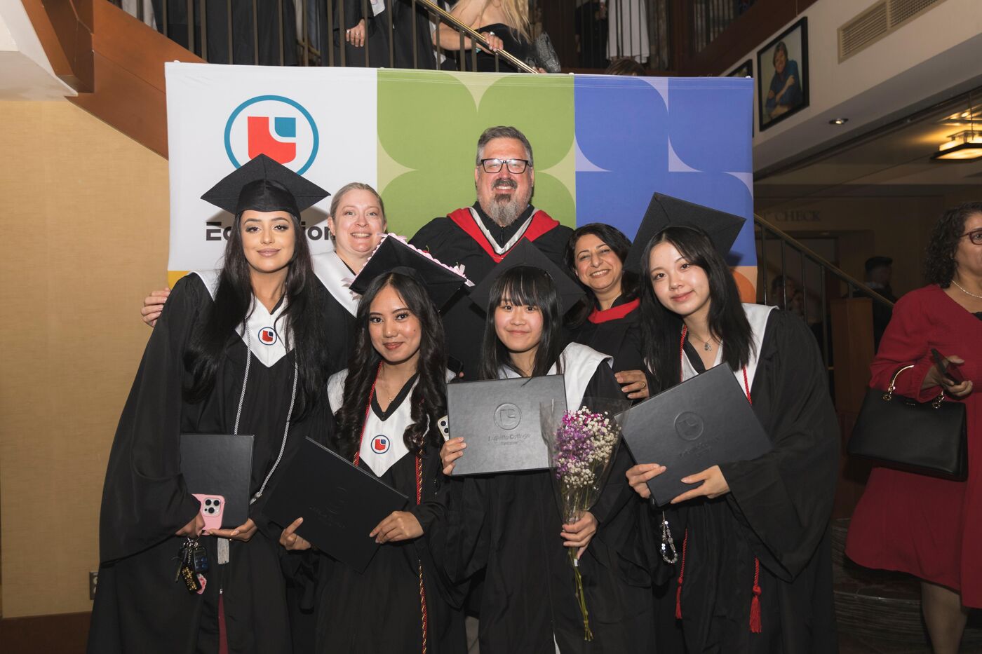 A group of smiling graduates in caps and gowns pose for a photo with their instructors, celebrating their academic achievements.