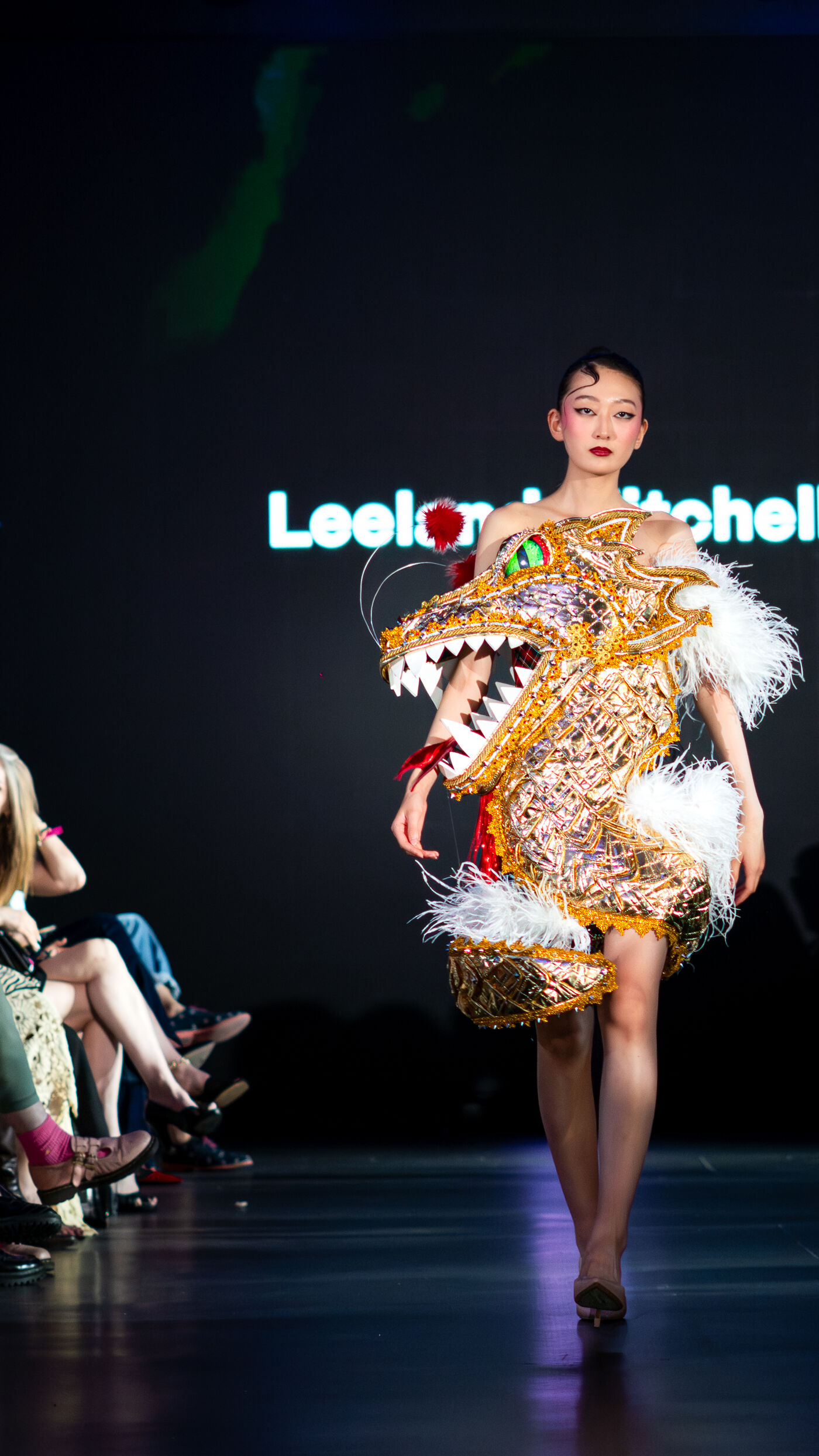 A model walks the runway in a spectacular golden dragon-shaped dress, featuring white feathers and striking details.
