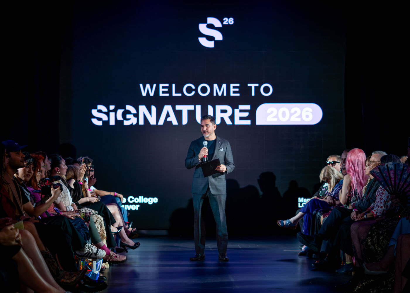 A man speaks on a stage in front of an audience, with a large "WELCOME TO SIGNATURE 2026" logo displayed behind him.