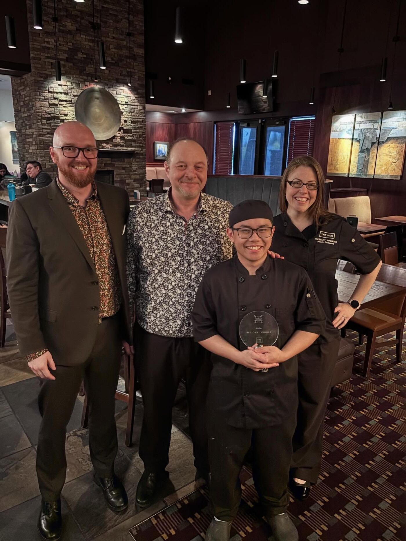 Four people pose for a photo inside a restaurant. One person is holding an award.