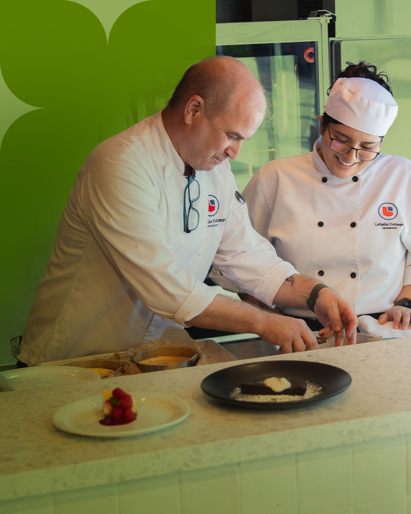 Two chefs, a man and a woman, are preparing desserts in a professional kitchen. The man is decorating a plate while the woman smiles.