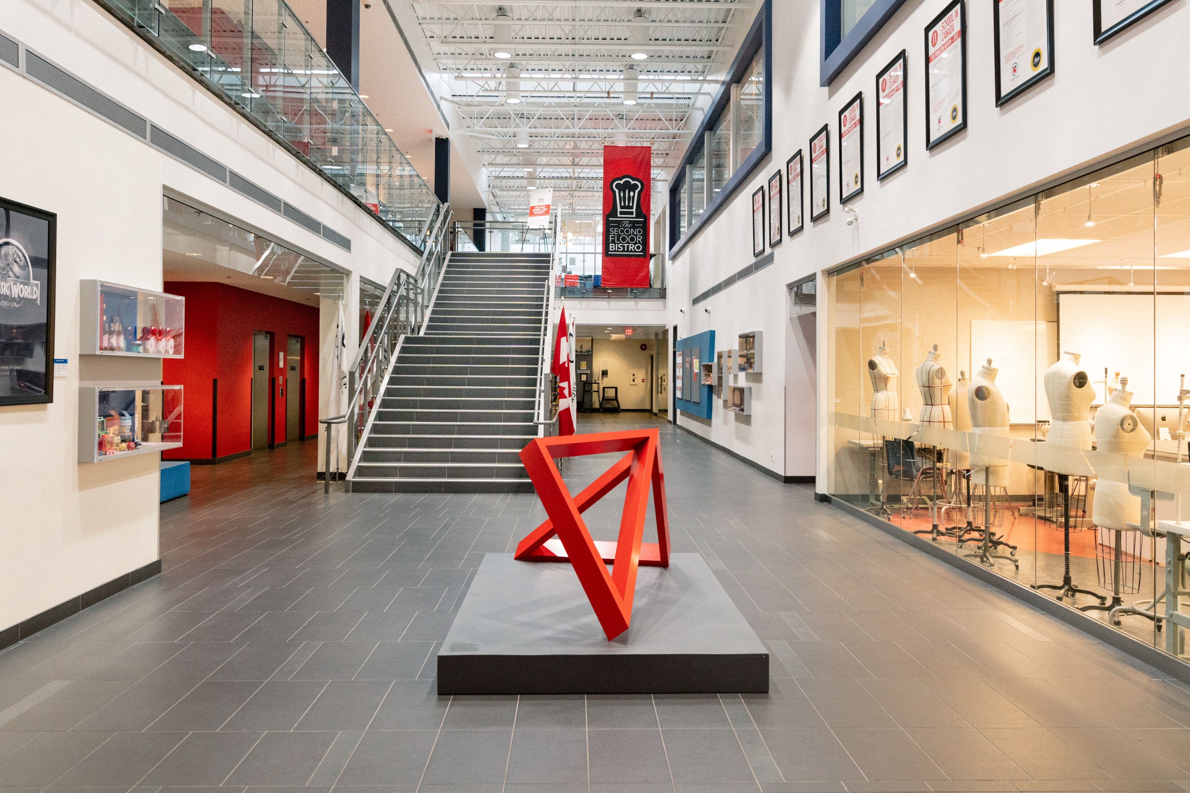 A spacious atrium with a striking red geometric sculpture, flanked by an art exhibit and a bistro sign.