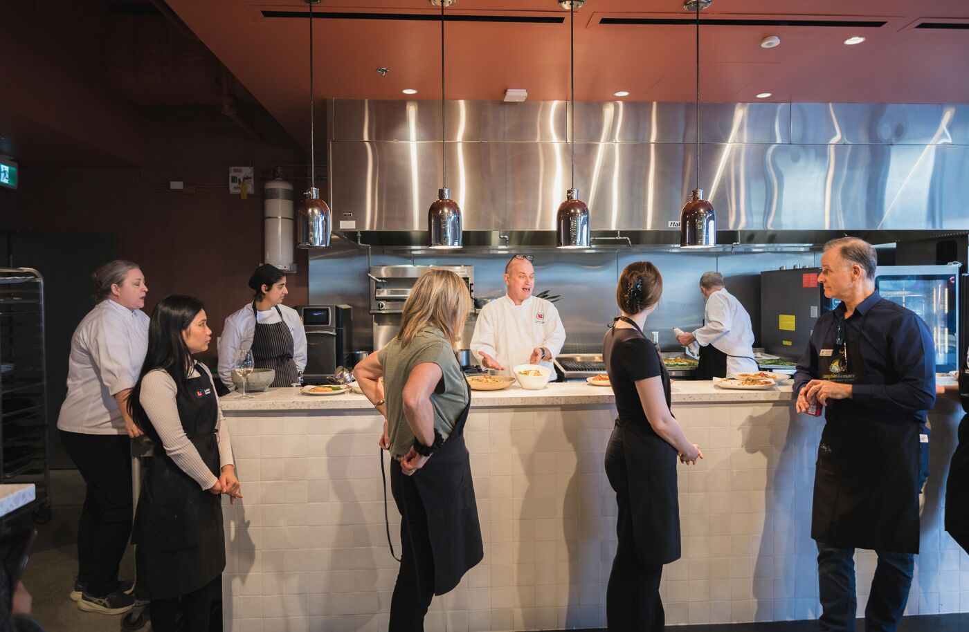 A group of people are watching a cooking demonstration in front of a counter with a chef preparing food.