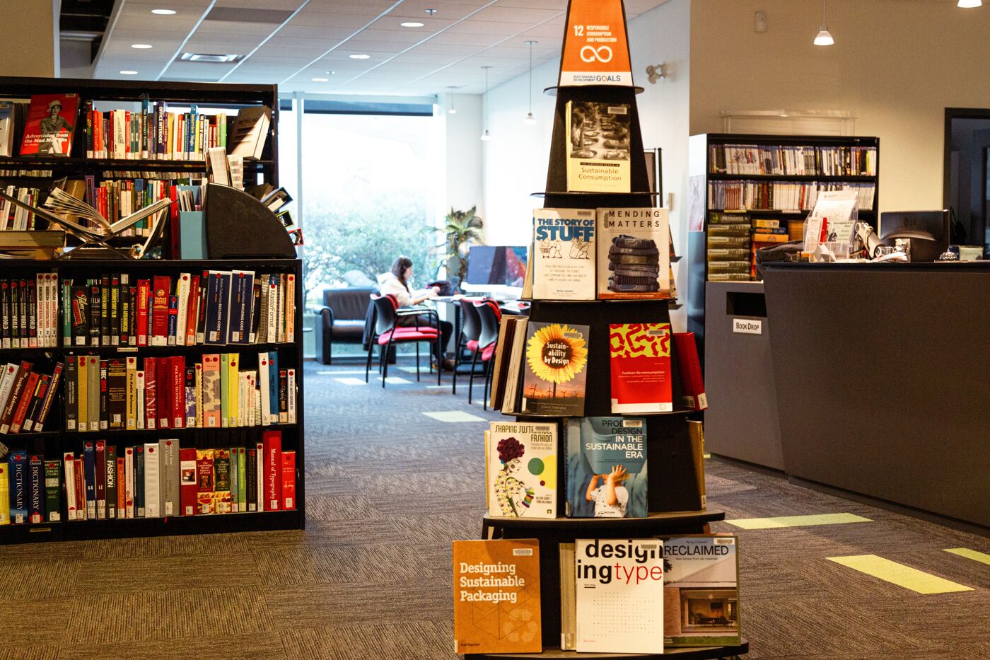 A student immersed in her studies in the tranquil corner of a library surrounded by books on sustainable design.