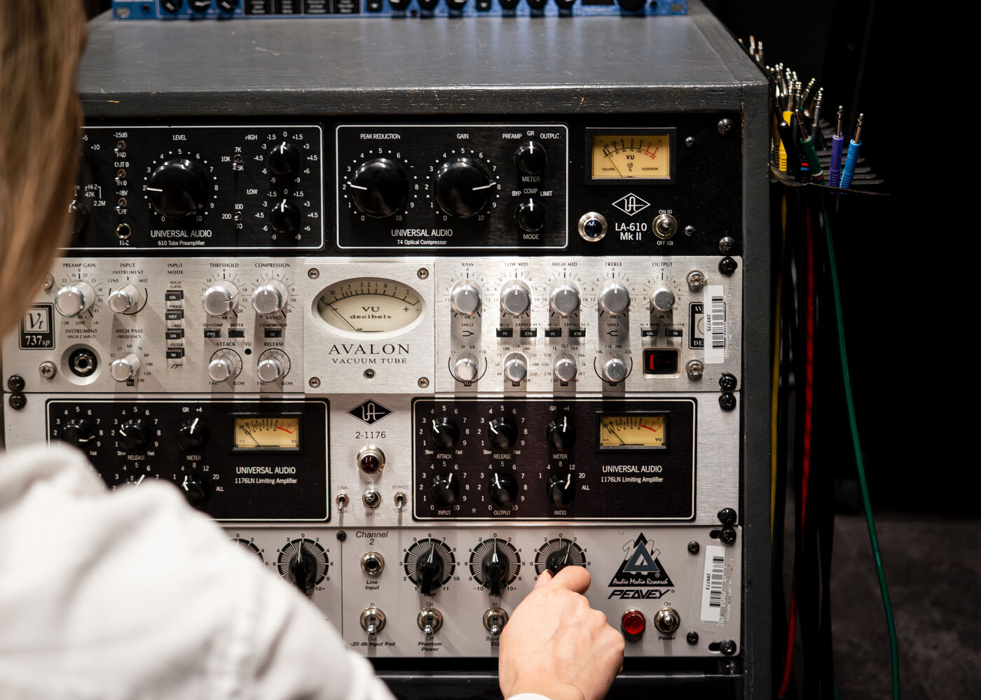 A person adjusts the controls on a rack of professional audio equipment, including preamplifiers and compressors, in a recording studio.