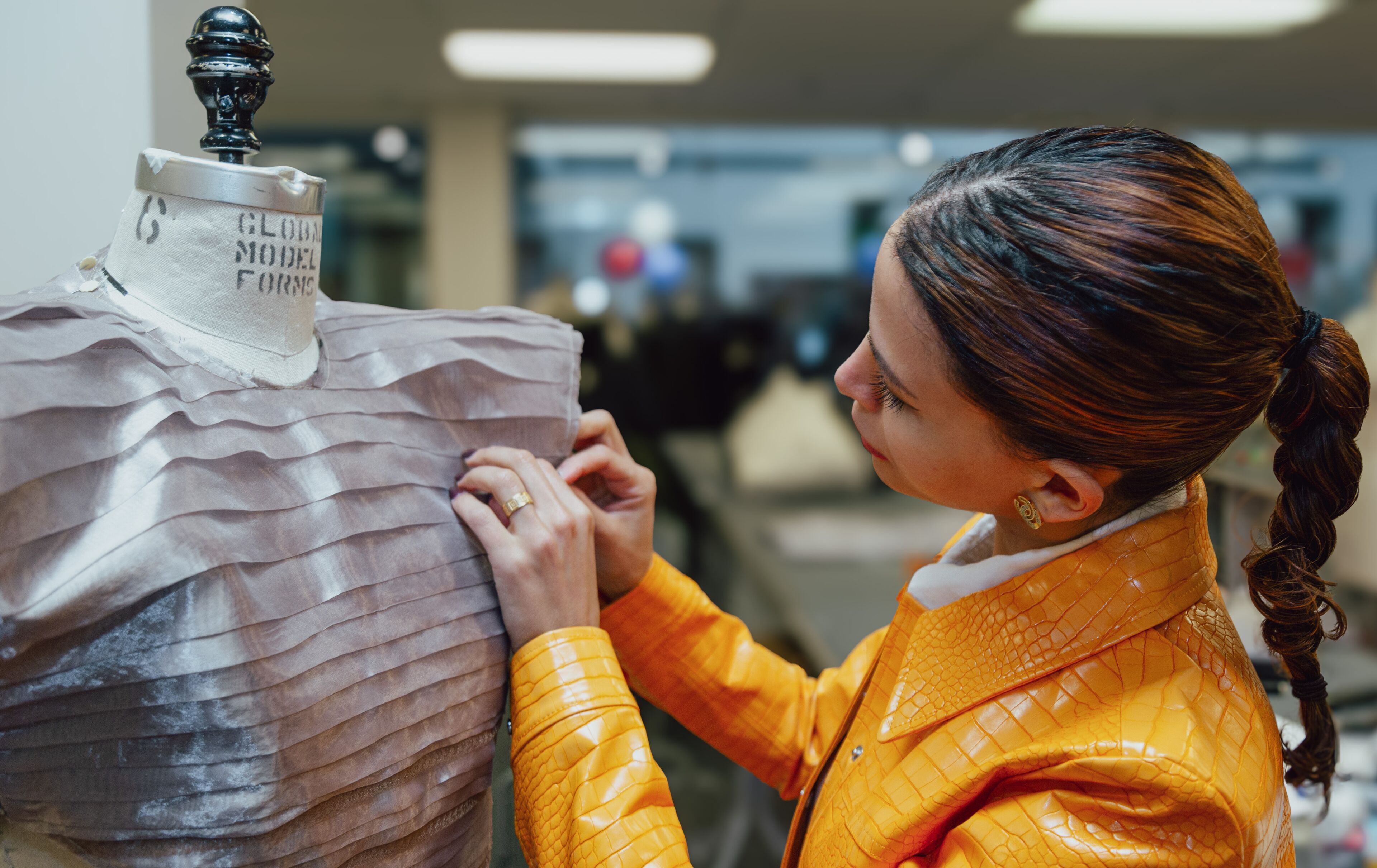 A designer meticulously adjusts the folds on a layered fabric dress on a mannequin, showcasing the careful art of fashion design.