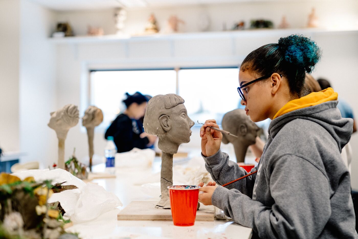 Artist carefully details a clay sculpture in a bright studio.