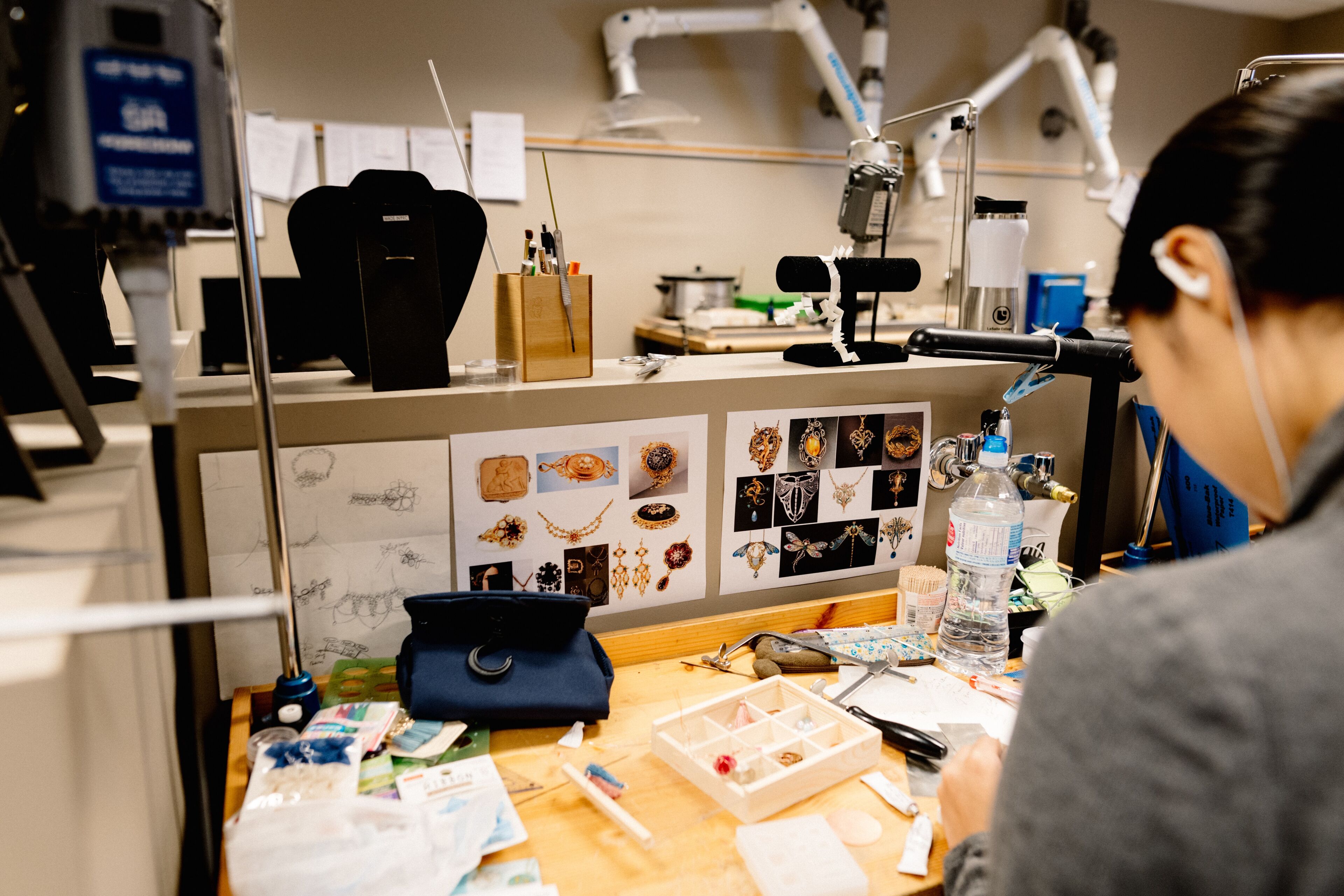 A jeweler meticulously assembles pieces amidst a workshop, surrounded by tools and designs.