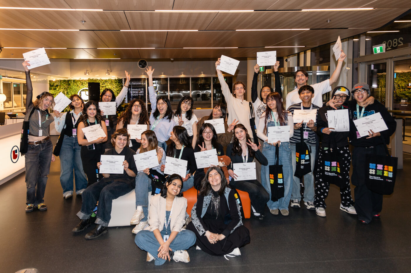 A group of students celebrates with certificates in an indoor event, smiling and holding up their awards for the camera.