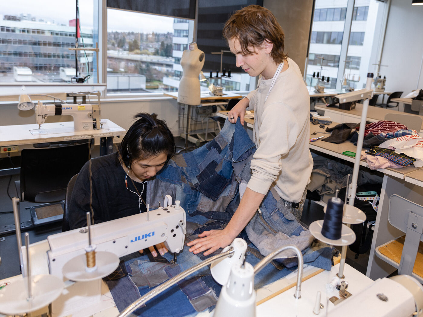 Two people are sewing a garment made of denim patches with a sewing machine.