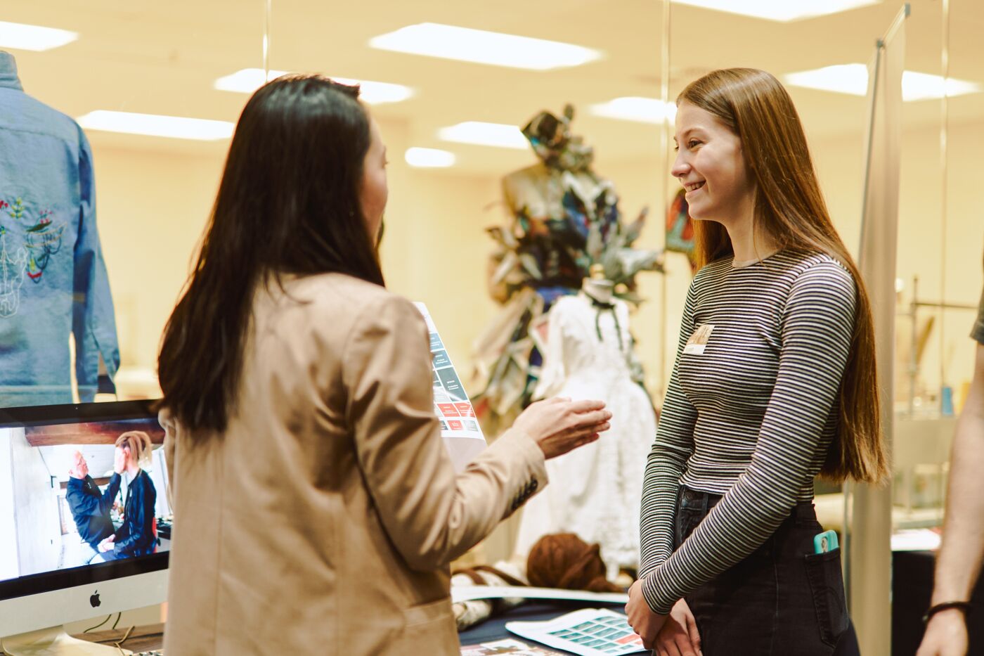 Two women engage in a lively discussion in a fashion design studio.