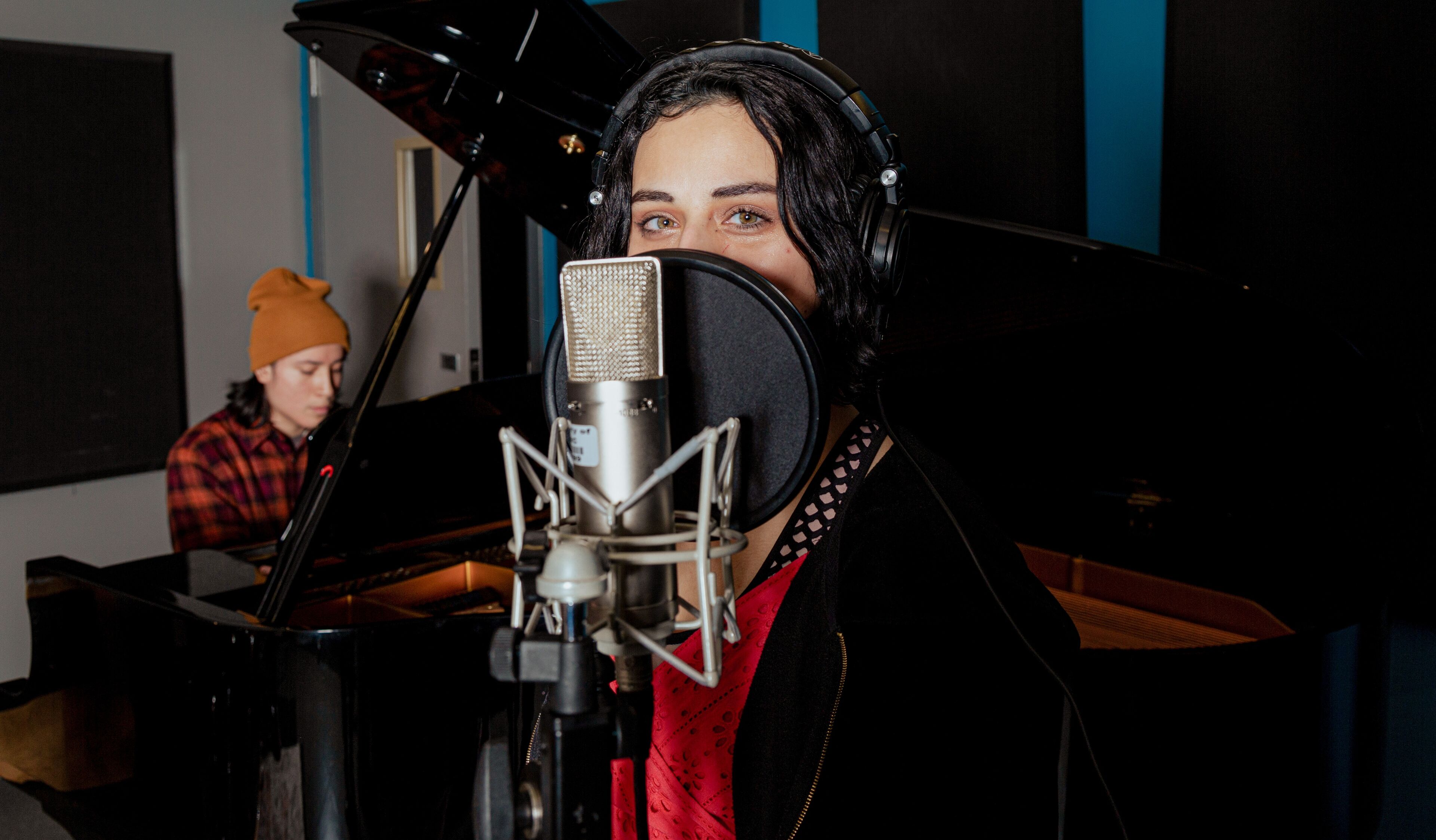 A vocalist recording vocals while a pianist accompanies in a soundproof studio.