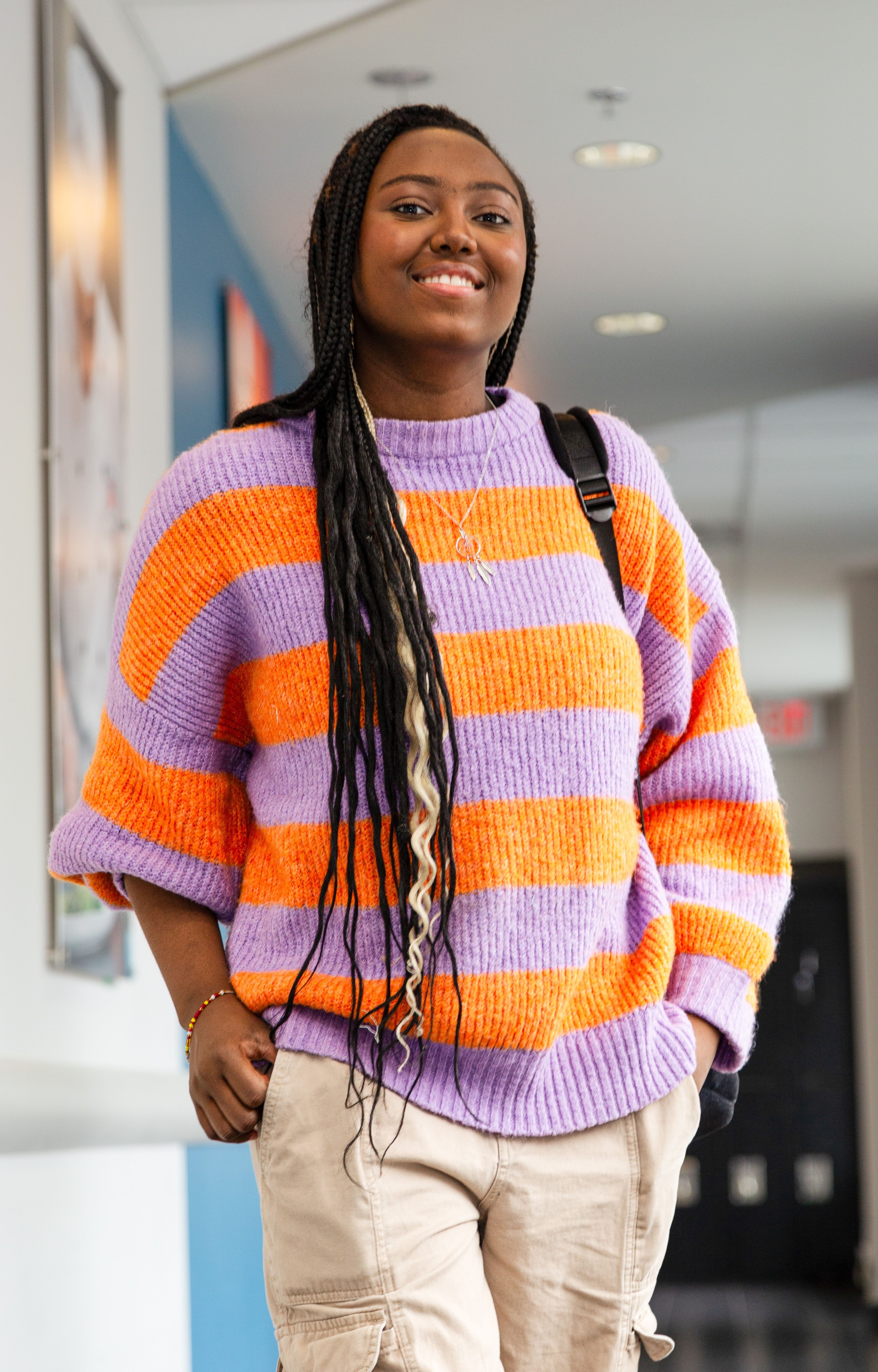 A young student in a colorful sweater radiates positivity in the campus hallway.