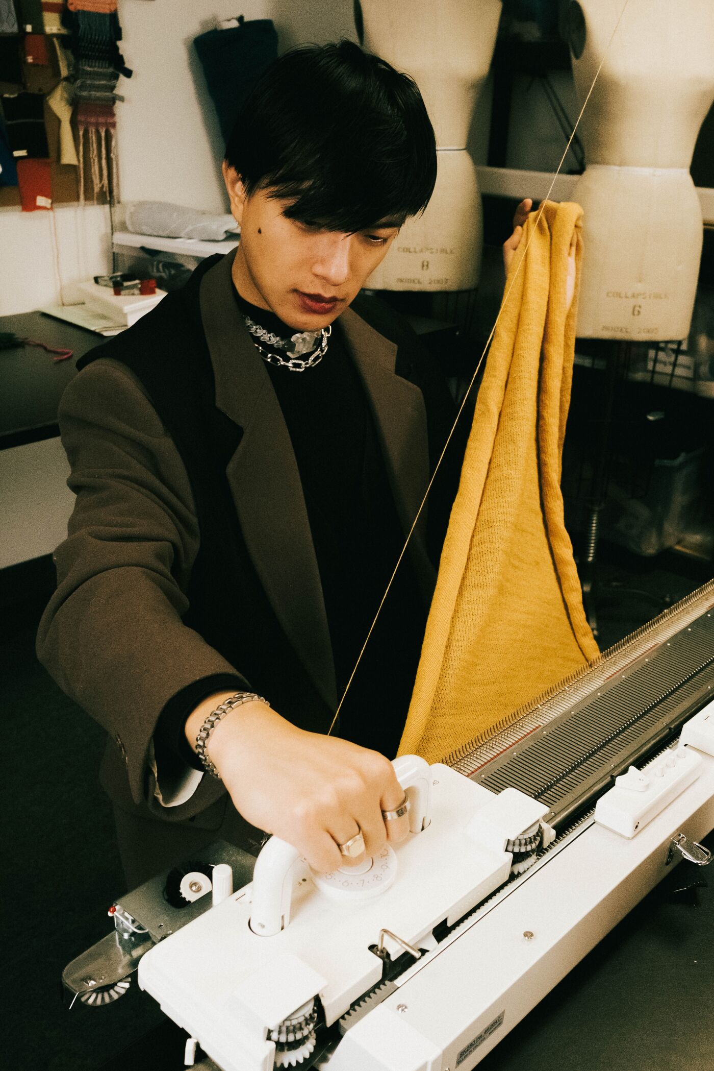 A focused artisan operates a knitting machine, creating a mustard-yellow fabric.