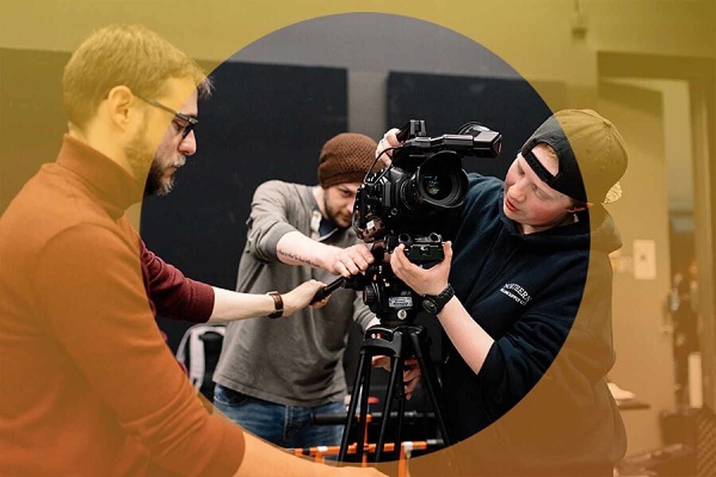 Three individuals collaboratively fine-tuning a professional video camera mounted on a tripod.