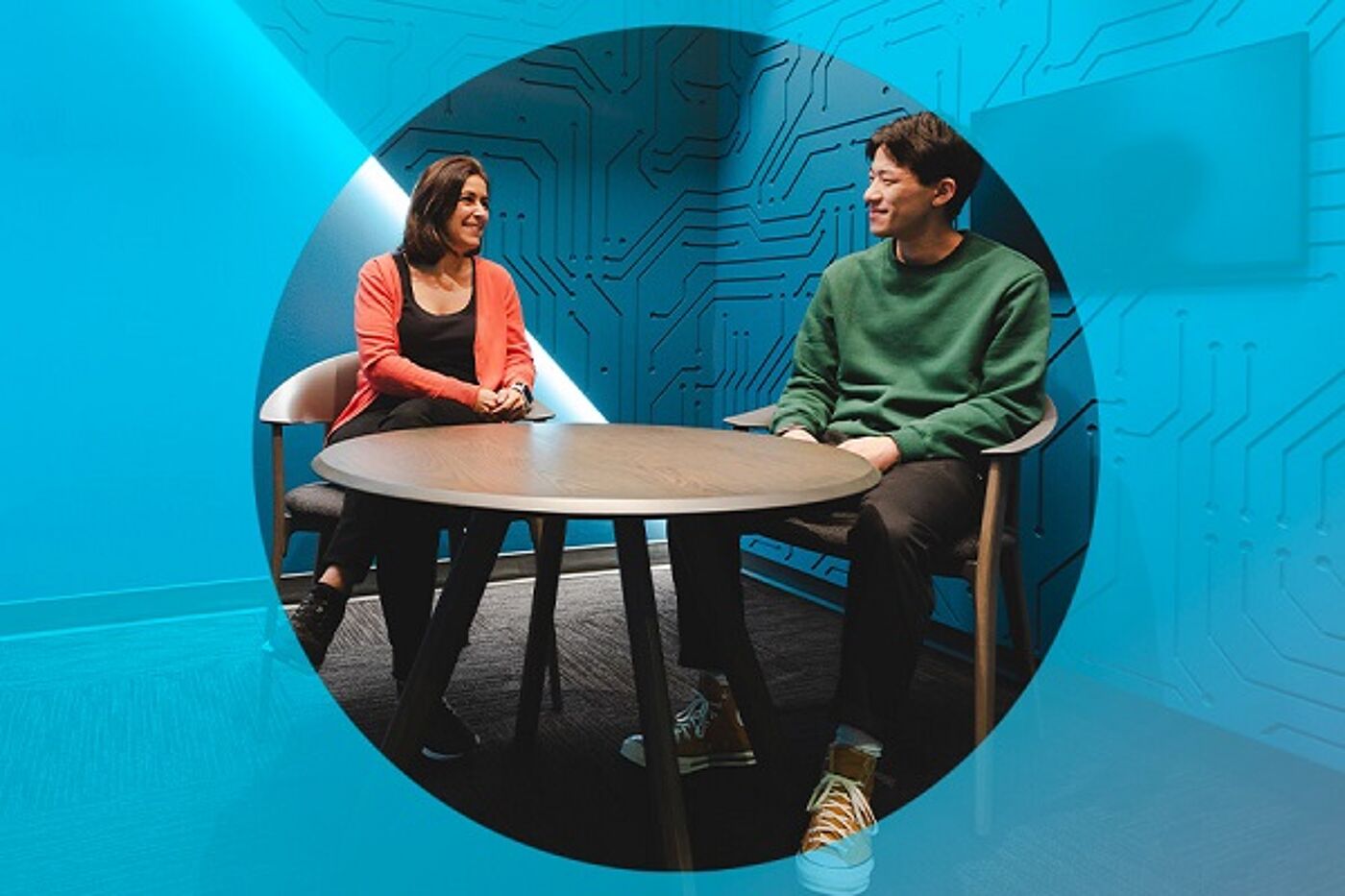 Two professionals engage in a relaxed conversation in a modern office space with abstract wall designs.