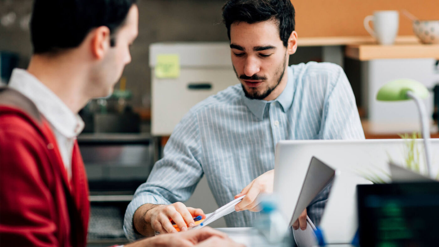 Two male colleagues discussing over documents in a casual office setting.