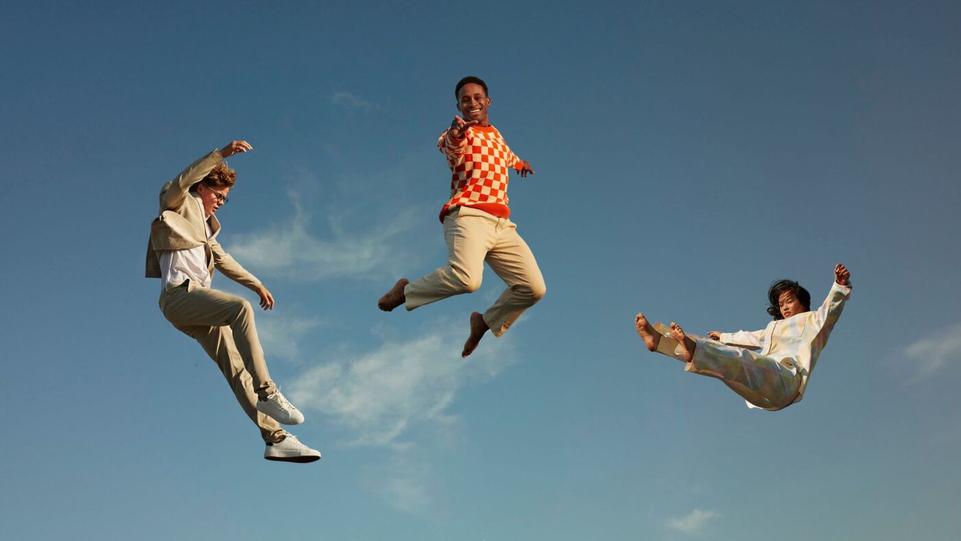 Three people, wearing different outfits, jump against a clear blue sky.