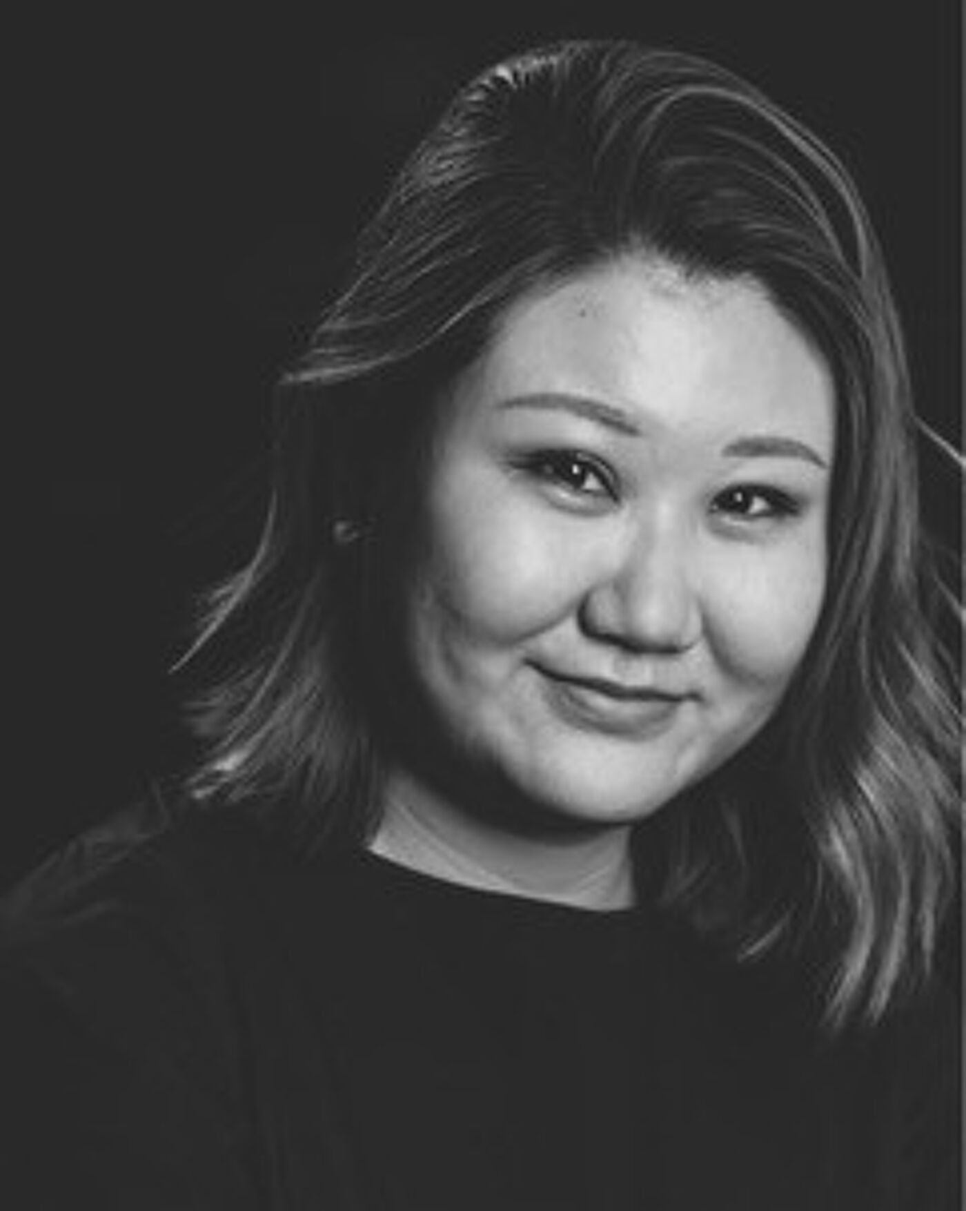Close-up black and white portrait of a woman with shoulder-length hair, smiling subtly.