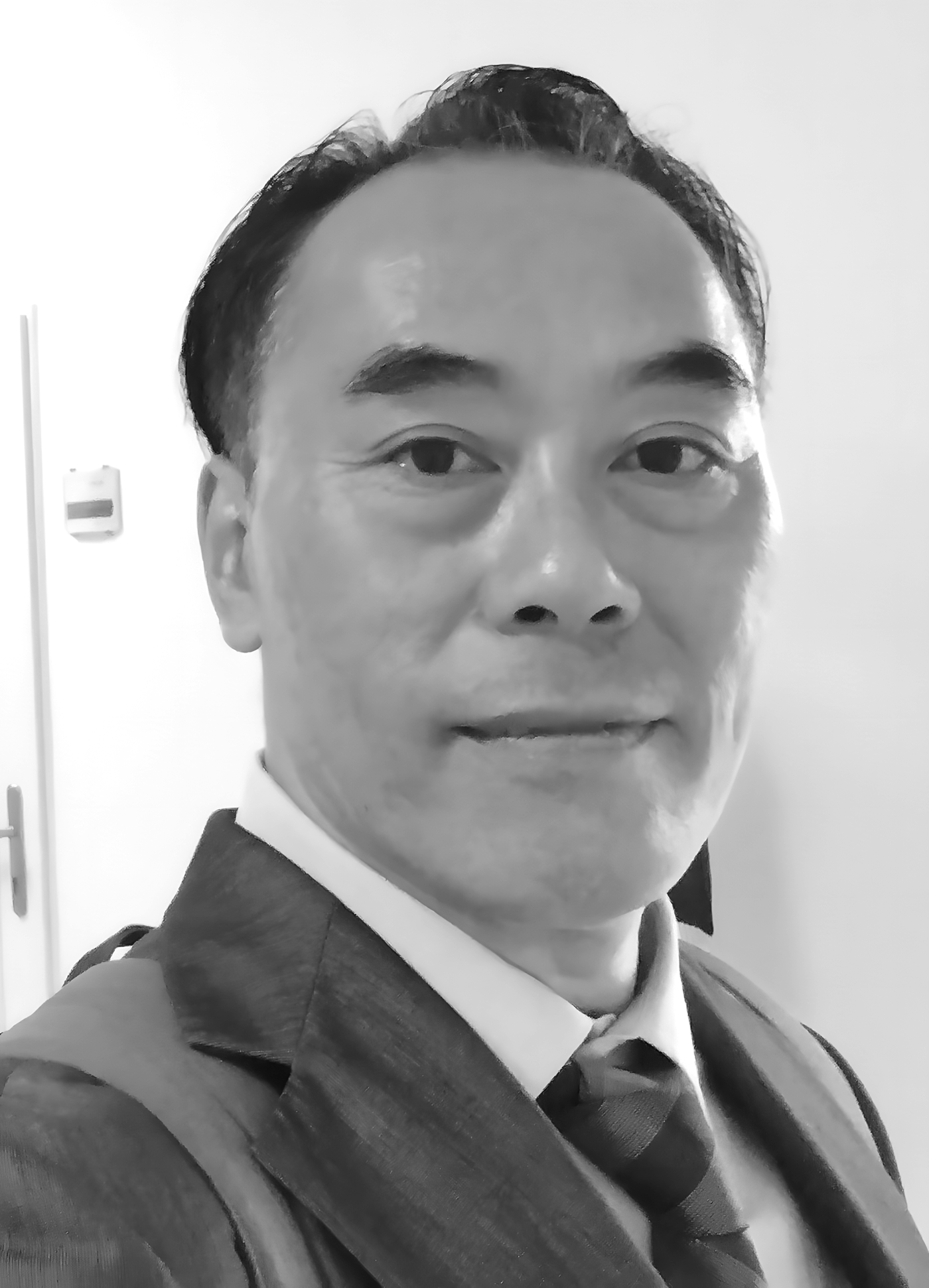 Close-up black and white portrait of a man in a suit and tie, his face showing subtle lines and a calm expression.