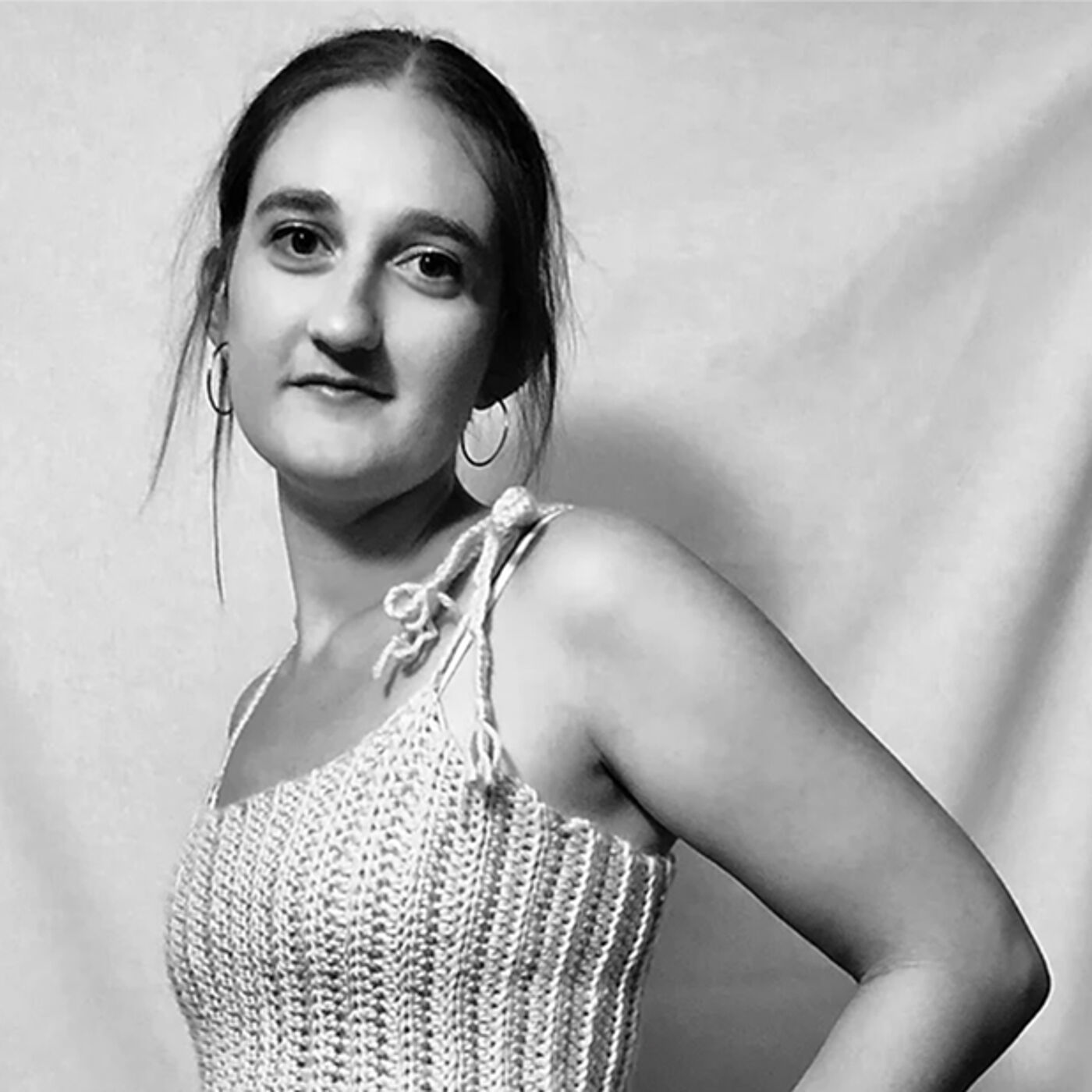 Close-up black and white shot of a young woman with shoulder-length hair, wearing a crocheted top with thin straps, looking slightly to her left.