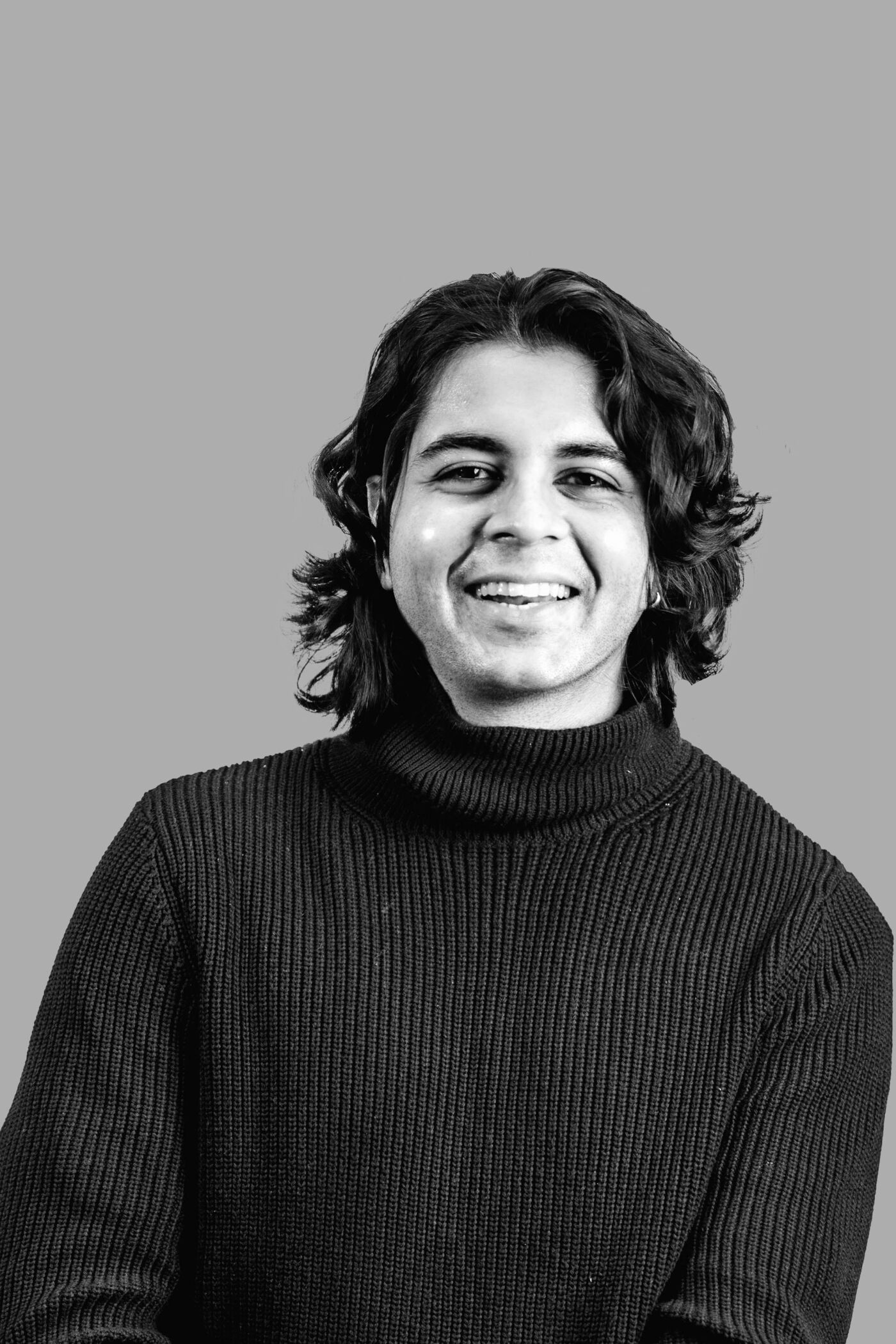 Close-up black and white shot of a smiling person with long, wavy hair wearing a turtleneck sweater.