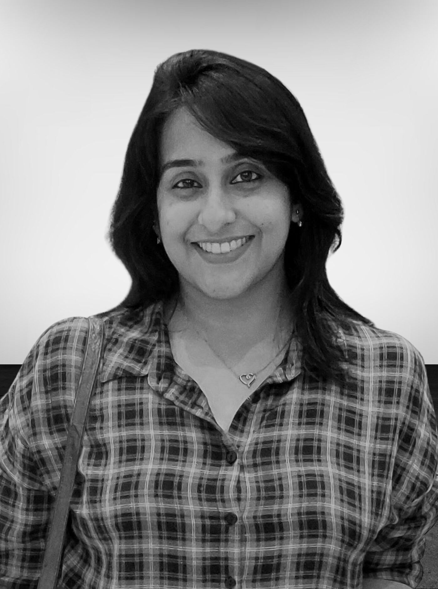 Close-up black and white shot of a woman with shoulder-length dark hair, wearing a plaid shirt and a simple necklace.