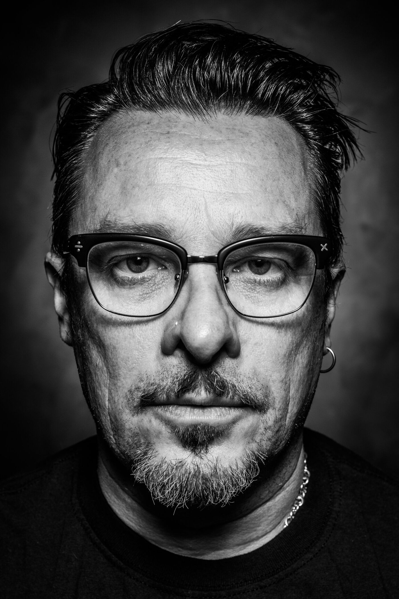 Close-up black and white portrait of a man with glasses, goatee, and short hair slicked back.