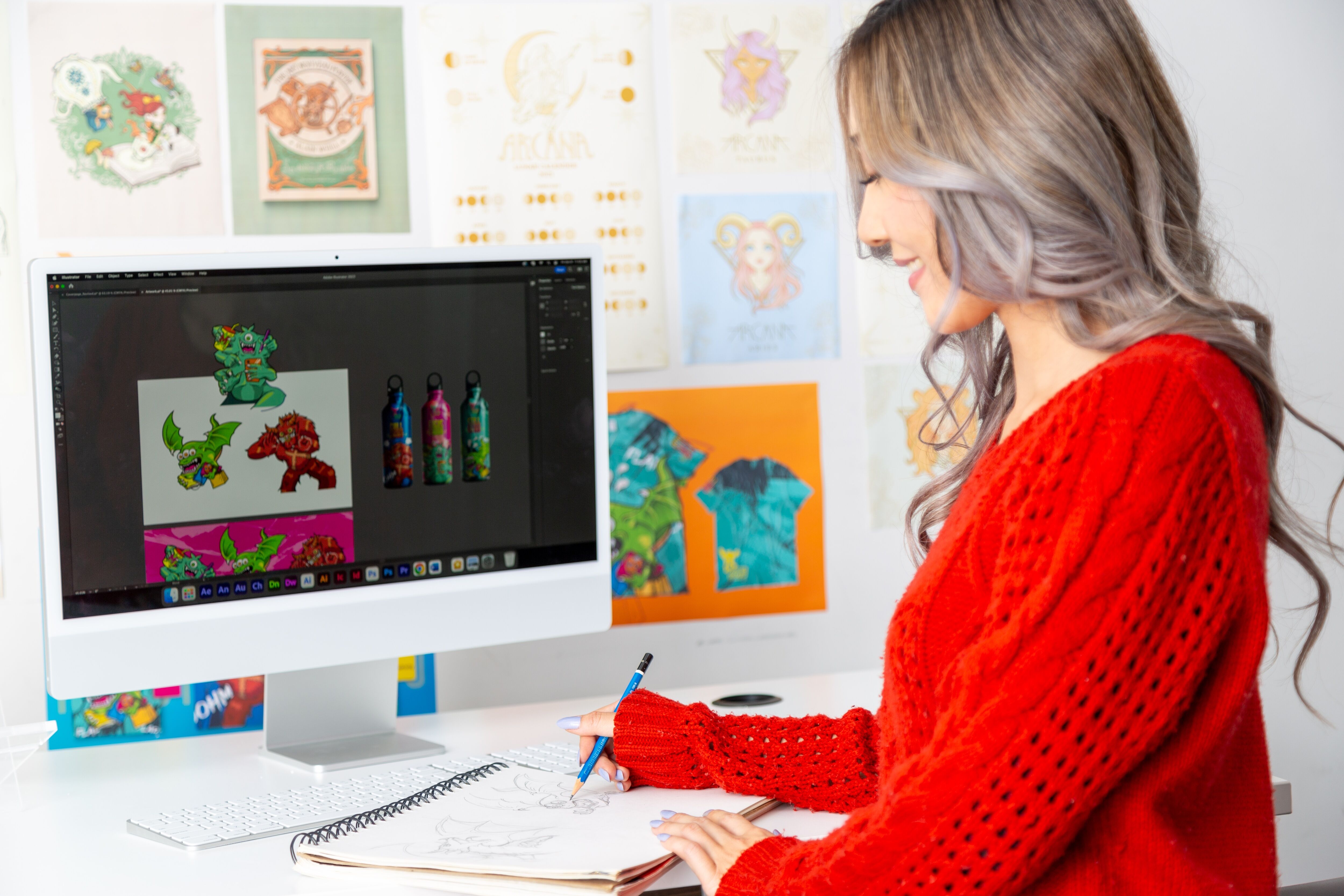  A woman in a red sweater creating digital art on a computer, surrounded by colorful illustrations.