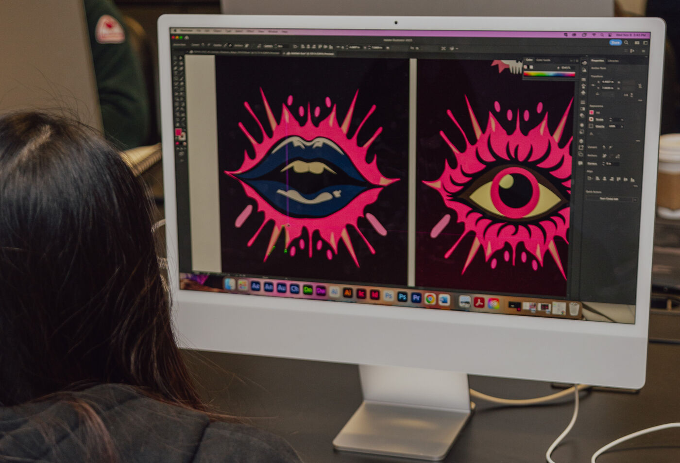 An artist focuses on a computer screen displaying bold digital illustrations of a lip and an eye in striking colors.
