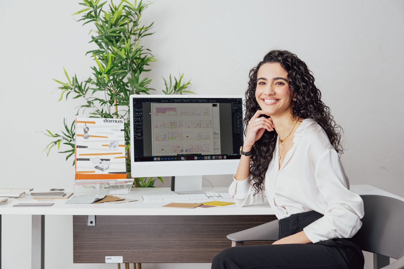 A joyful designer poses at her workspace, surrounded by plans and inspiration.