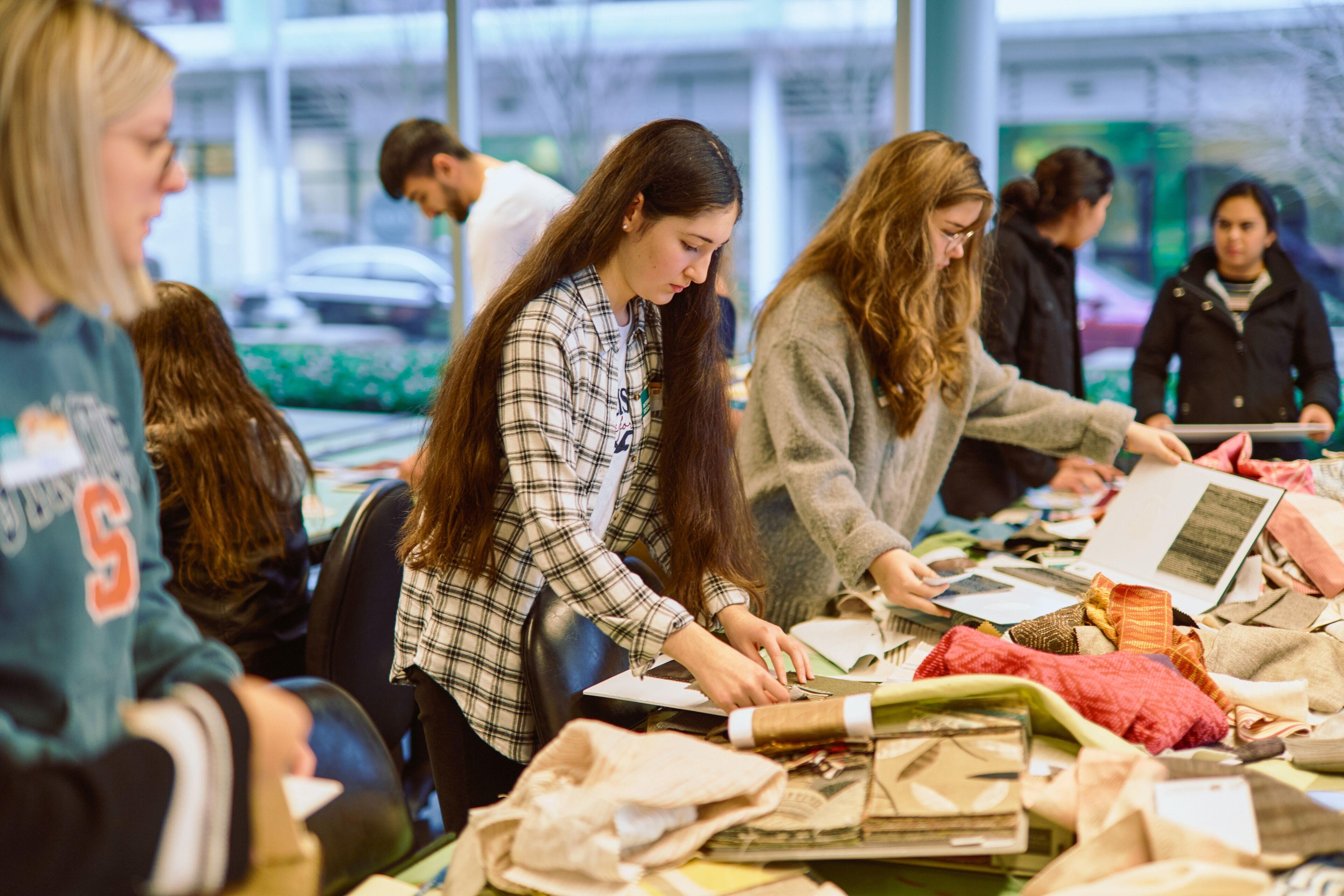 Fashion design students actively engaged in selecting fabrics and discussing projects in a vibrant workshop environment.