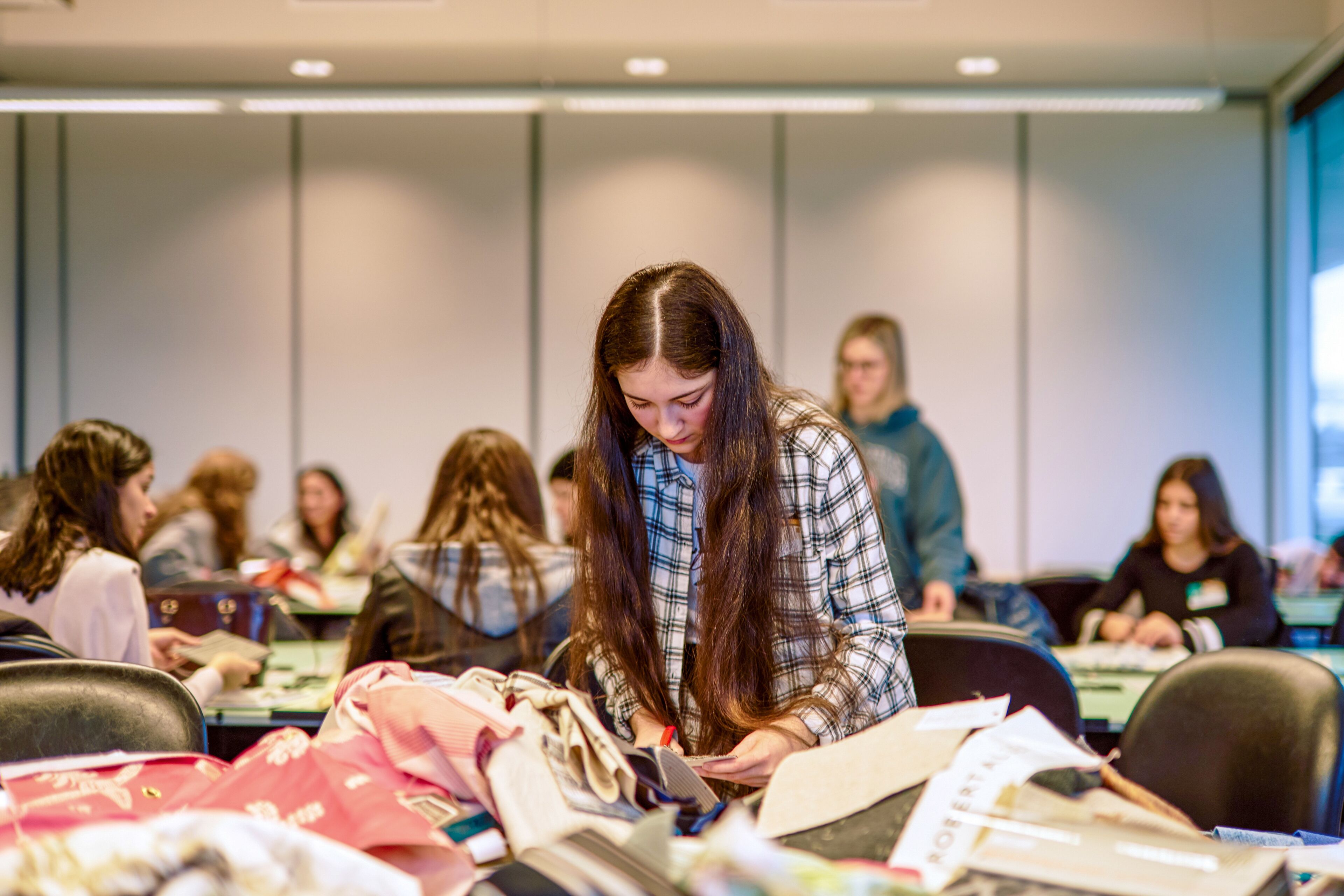 A dedicated fashion design student meticulously selects materials amidst a busy classroom setting.